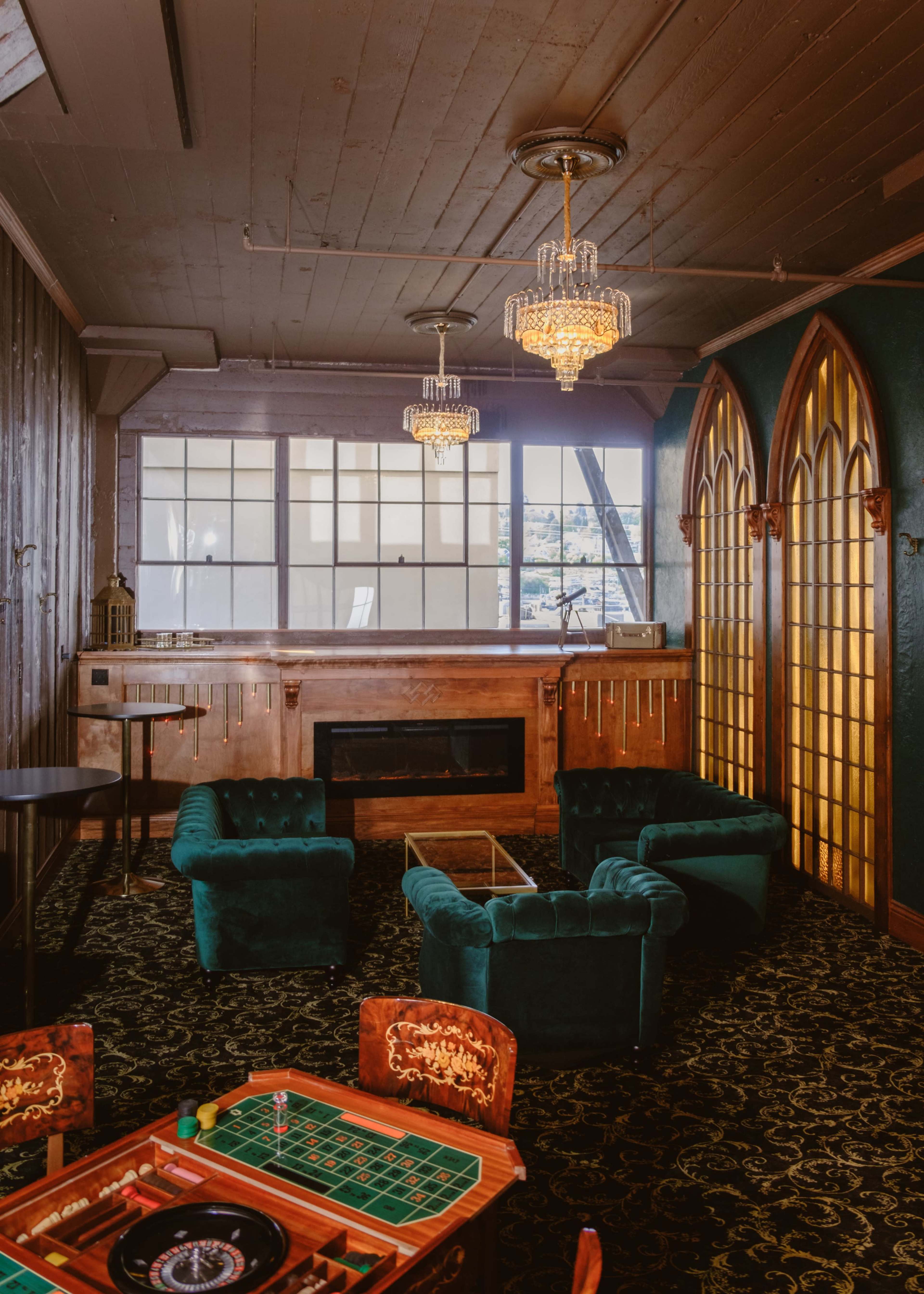A stylish lounge area features green velvet furniture, a glass coffee table, and ornate chandeliers, with a large window providing natural light.