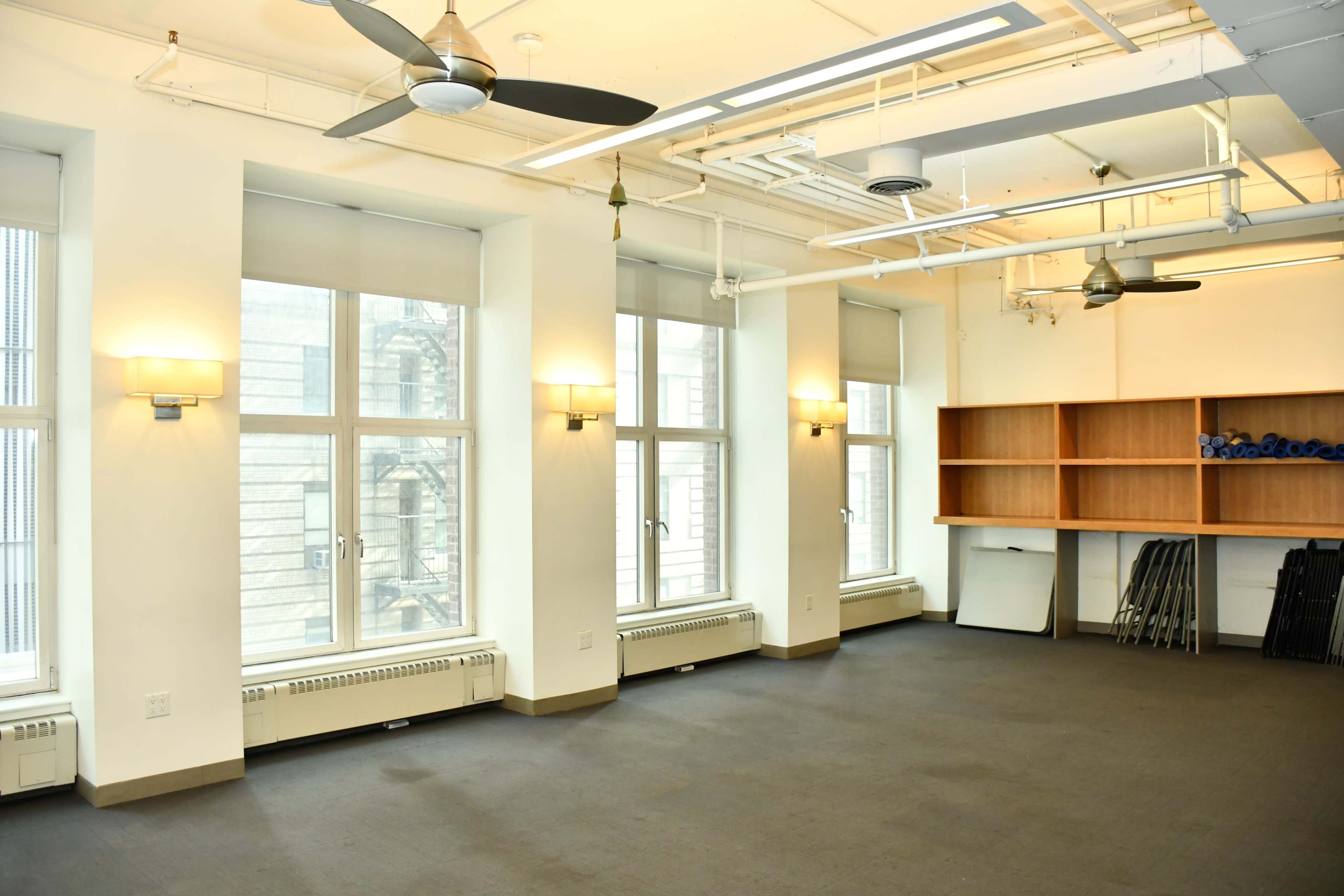 An empty room with large windows, overhead fans, and shelves against one wall.