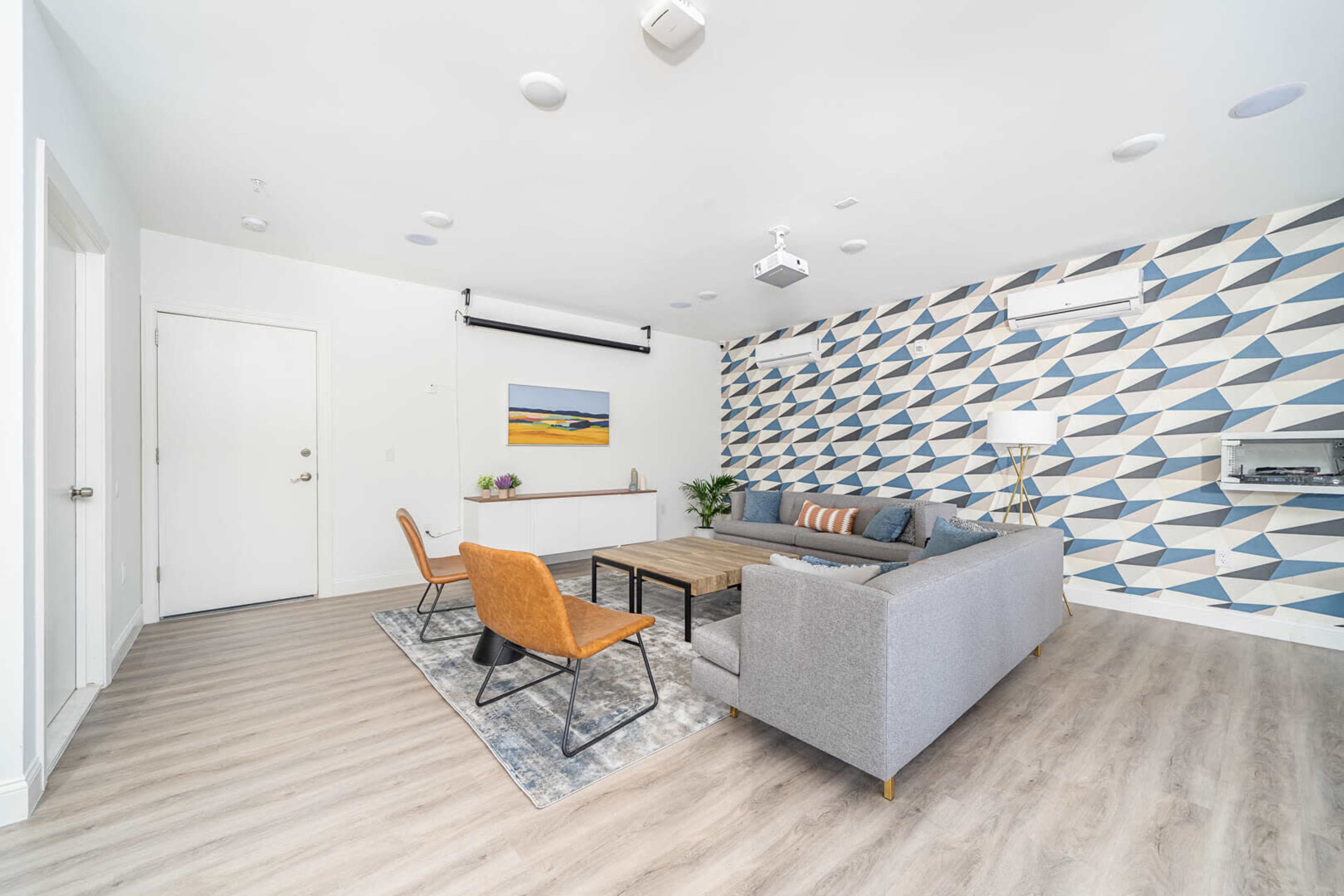 The room features a modern seating area with a gray sofa, orange chairs, and a geometric patterned accent wall.
