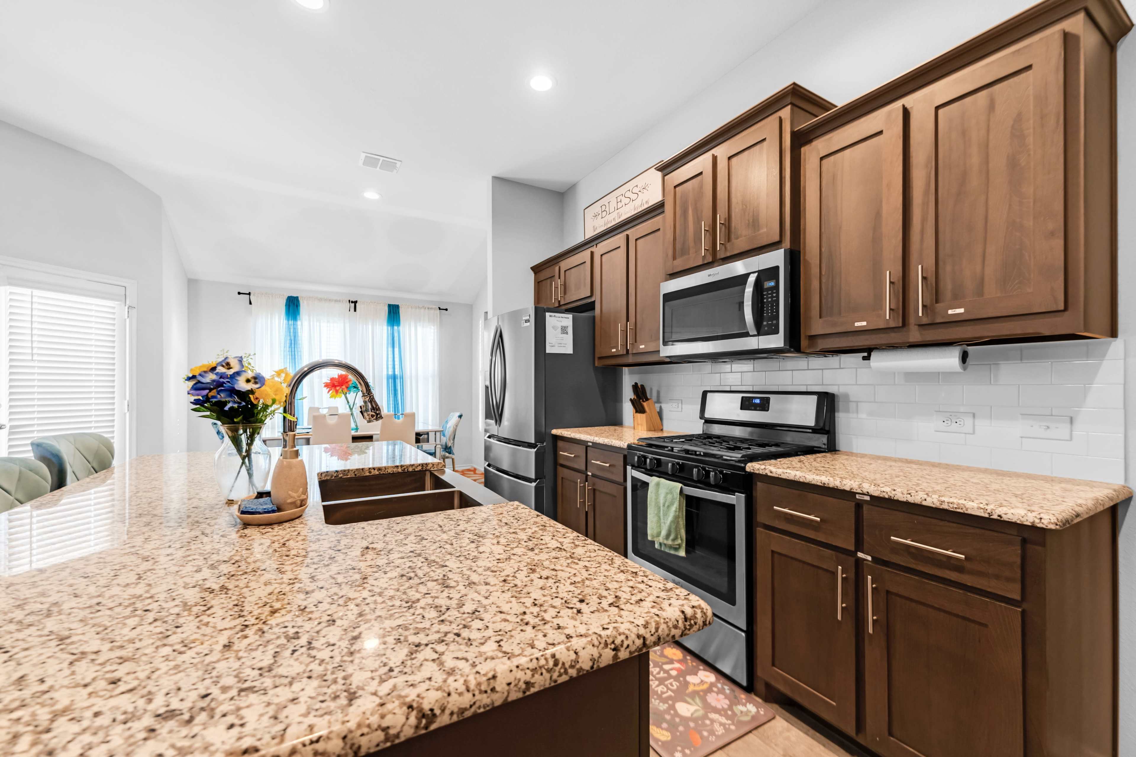 The kitchen features dark wooden cabinets, stainless steel appliances, and a granite countertop with a decorative island and a vase of flowers.