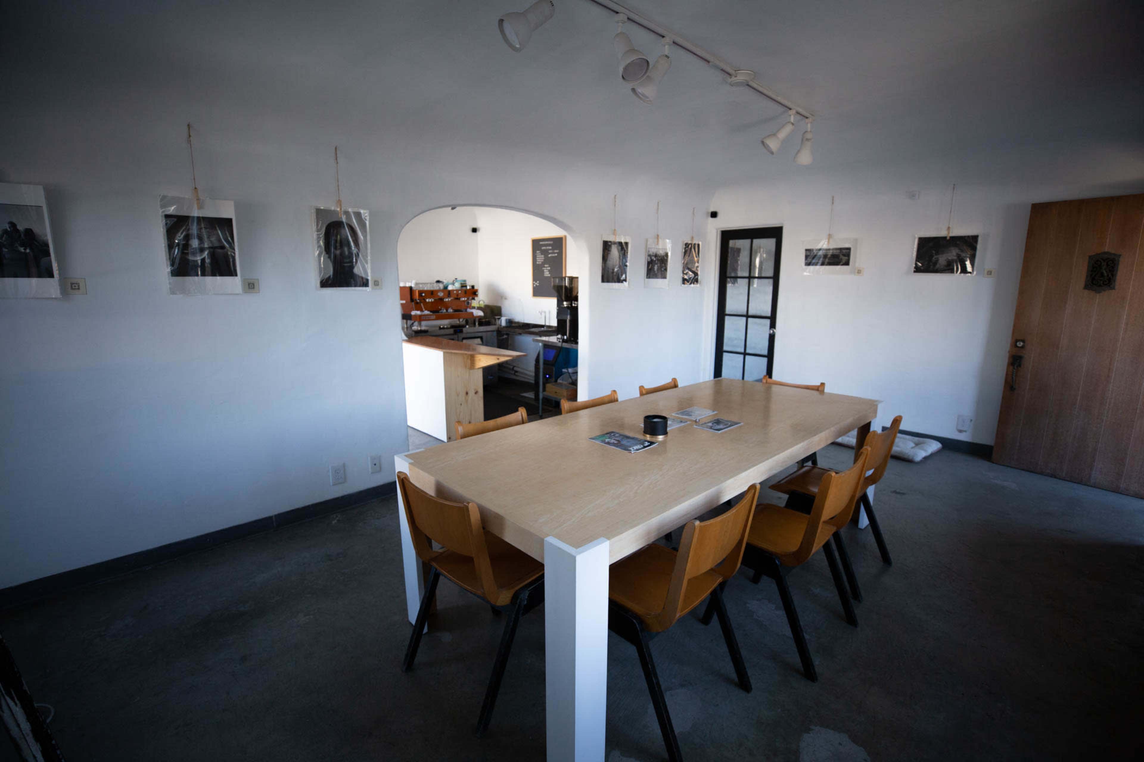 A long wooden table with eight chairs is positioned in a minimalist room featuring black and white photographs hung on the walls.