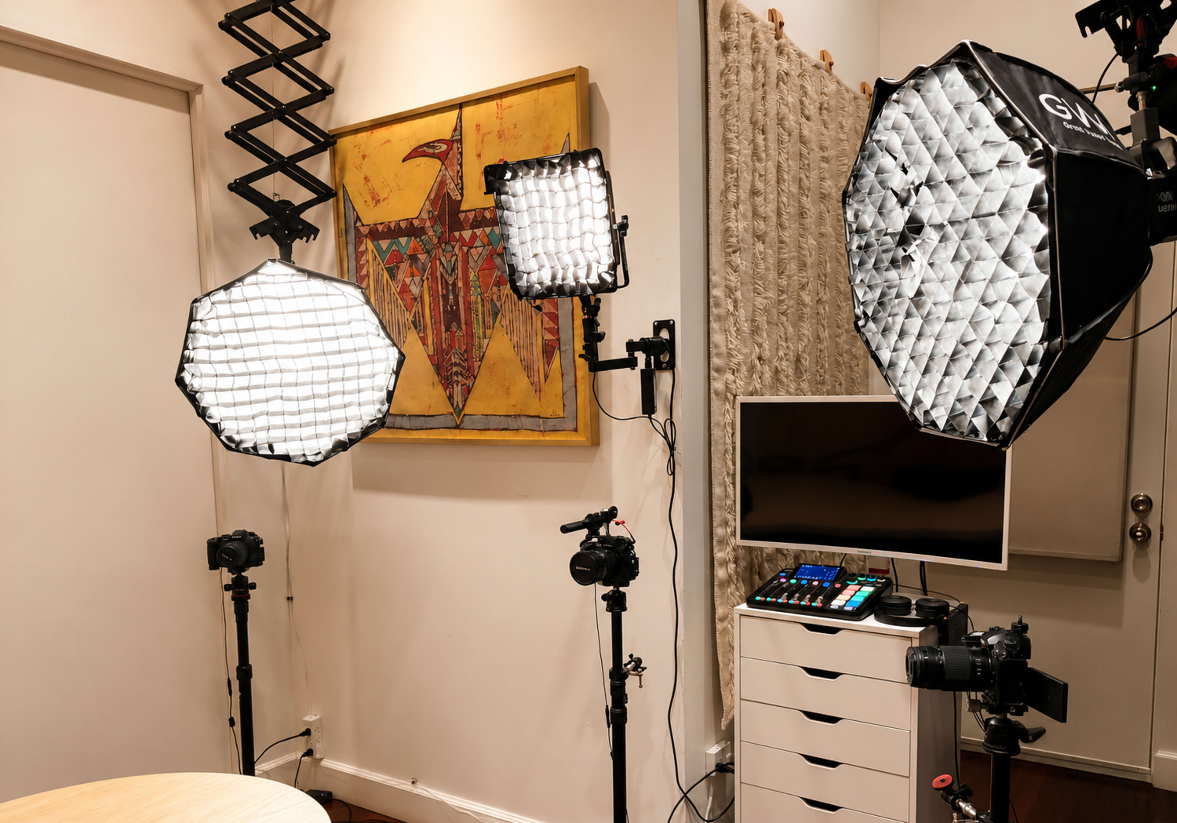 The image shows a well-lit indoor studio setup with two large softbox lights, multiple cameras on tripods, a monitor, and a decorative wall art piece.
