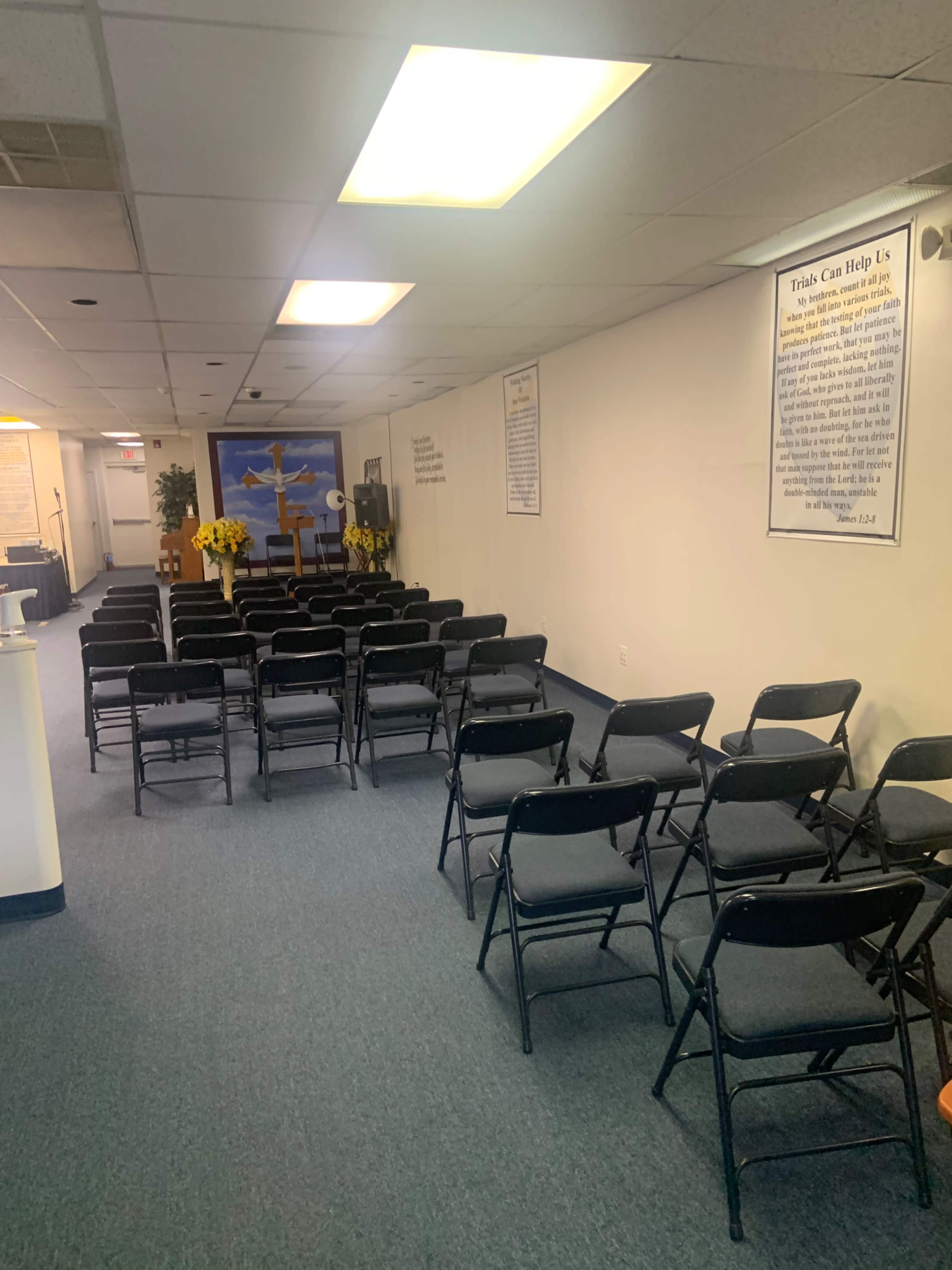 A row of black chairs arranged in a neatly organized, mostly empty room with a wall featuring motivational posters and a stage area in the background.