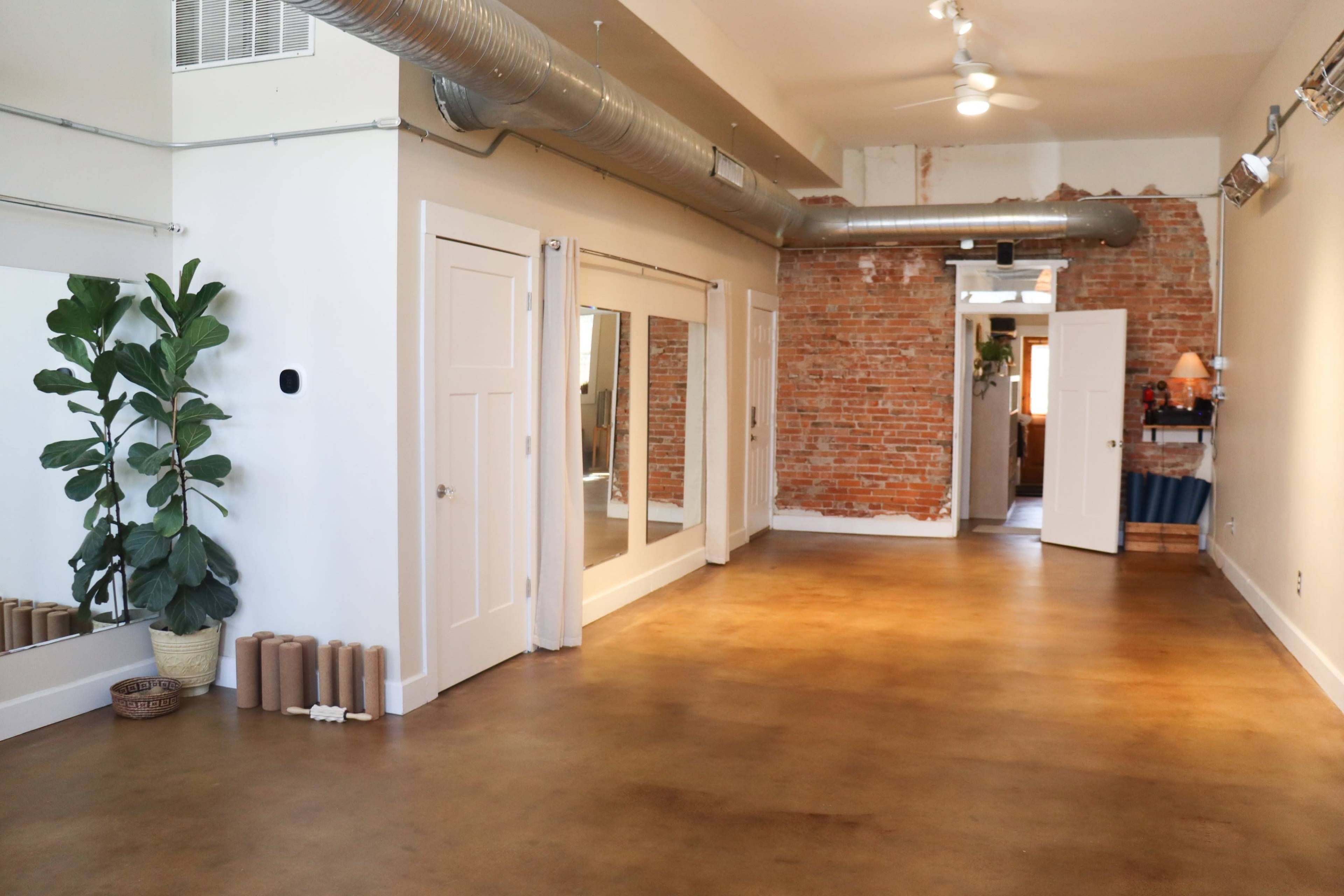 A spacious room with exposed brick walls, large mirrors, and a plant in the corner.