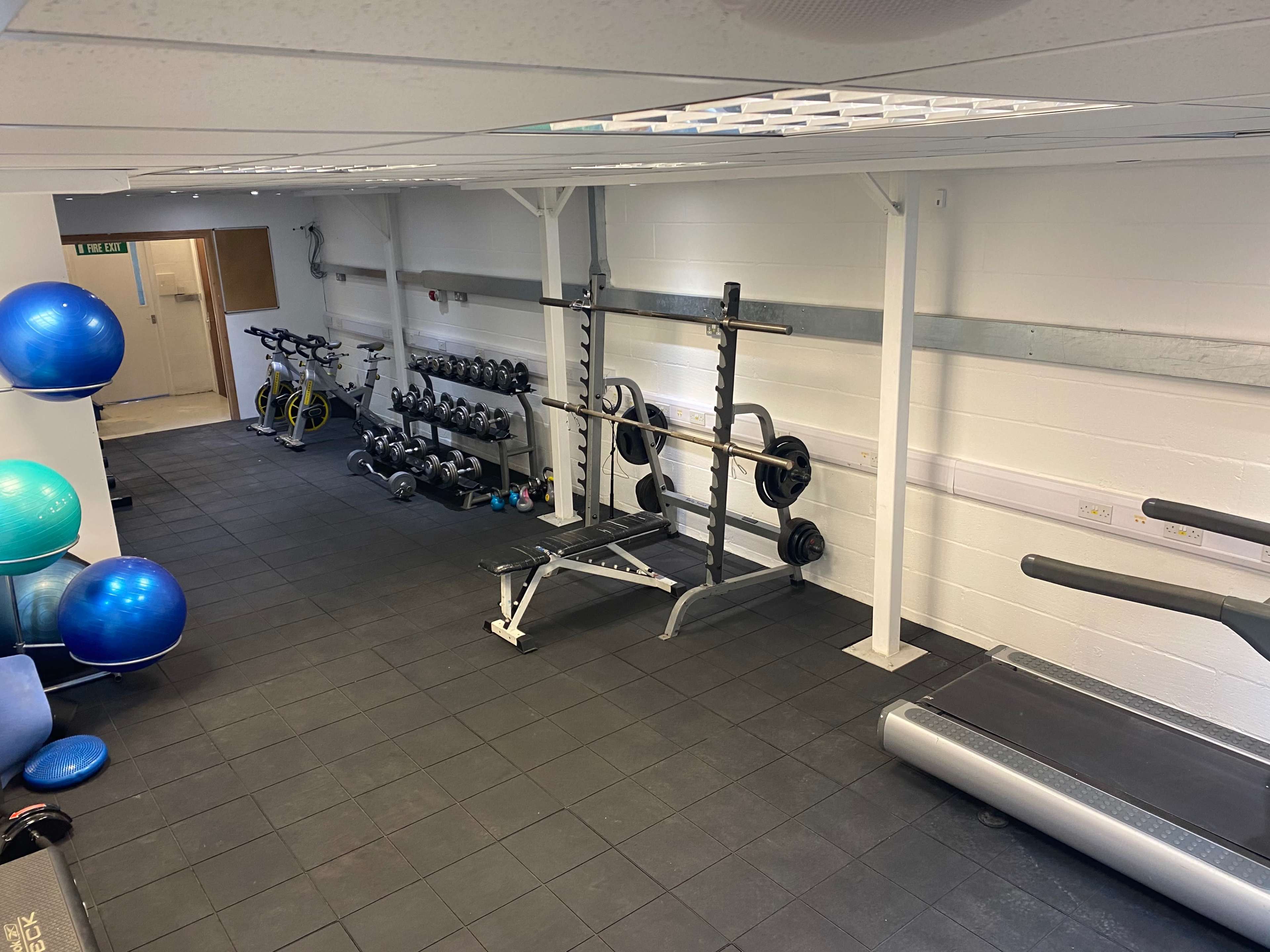 A gym interior featuring weightlifting equipment, exercise balls, and cardio machines on a black rubber floor.