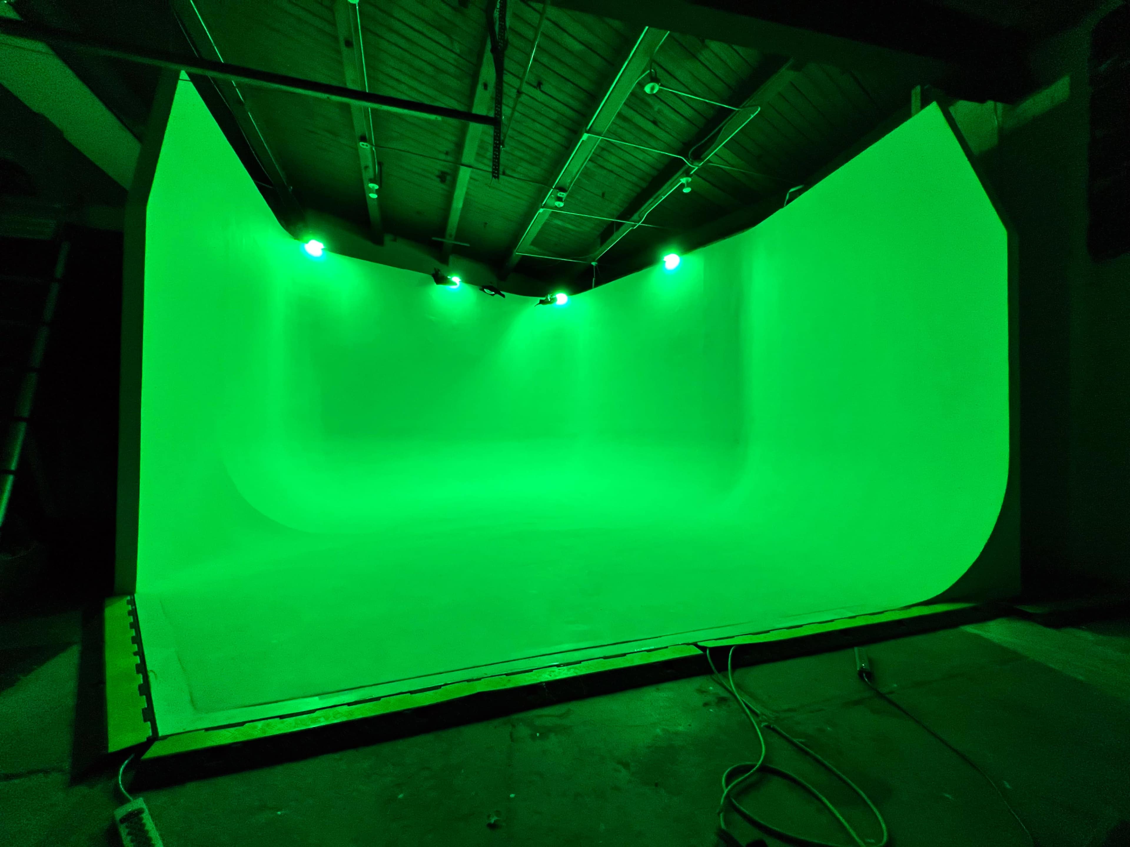 An empty studio space with a green curved backdrop and overhead lighting.