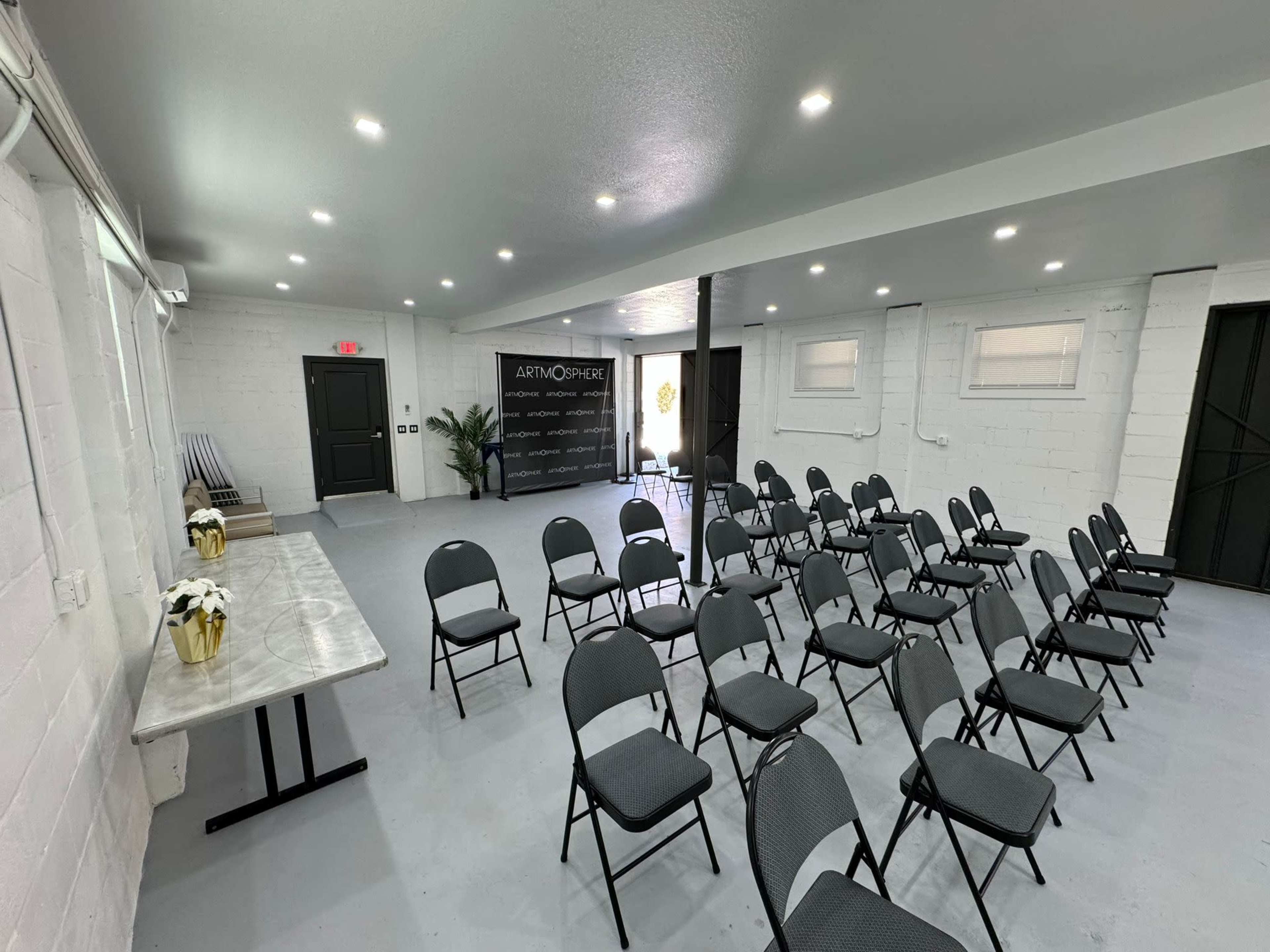 A conference room setup with several rows of black chairs facing a presentation area, featuring a marble table and a backdrop with "ARTMOSPHERE" on the wall.
