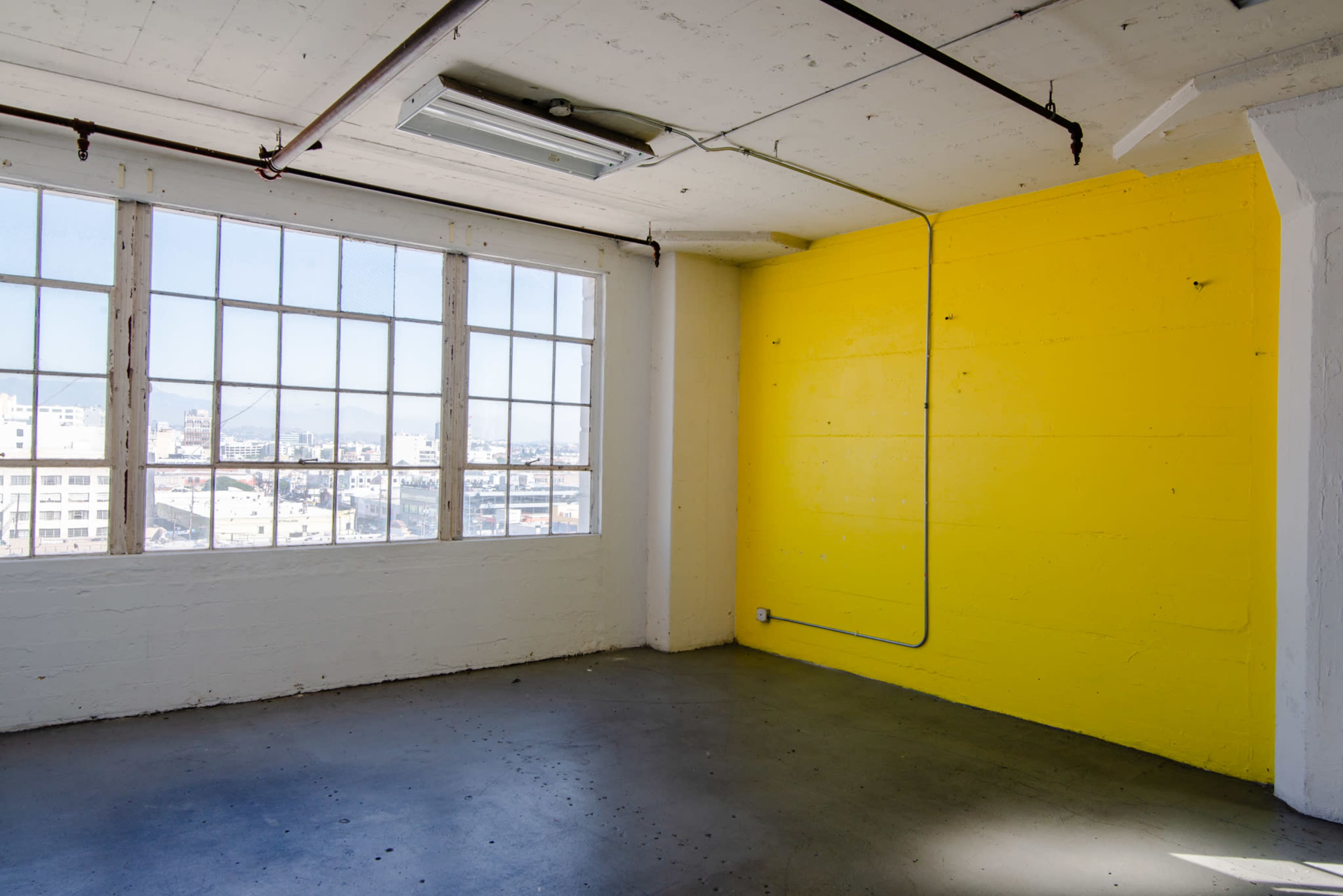 A bright yellow wall contrasts with the white walls in a spacious room with large windows overlooking a cityscape.