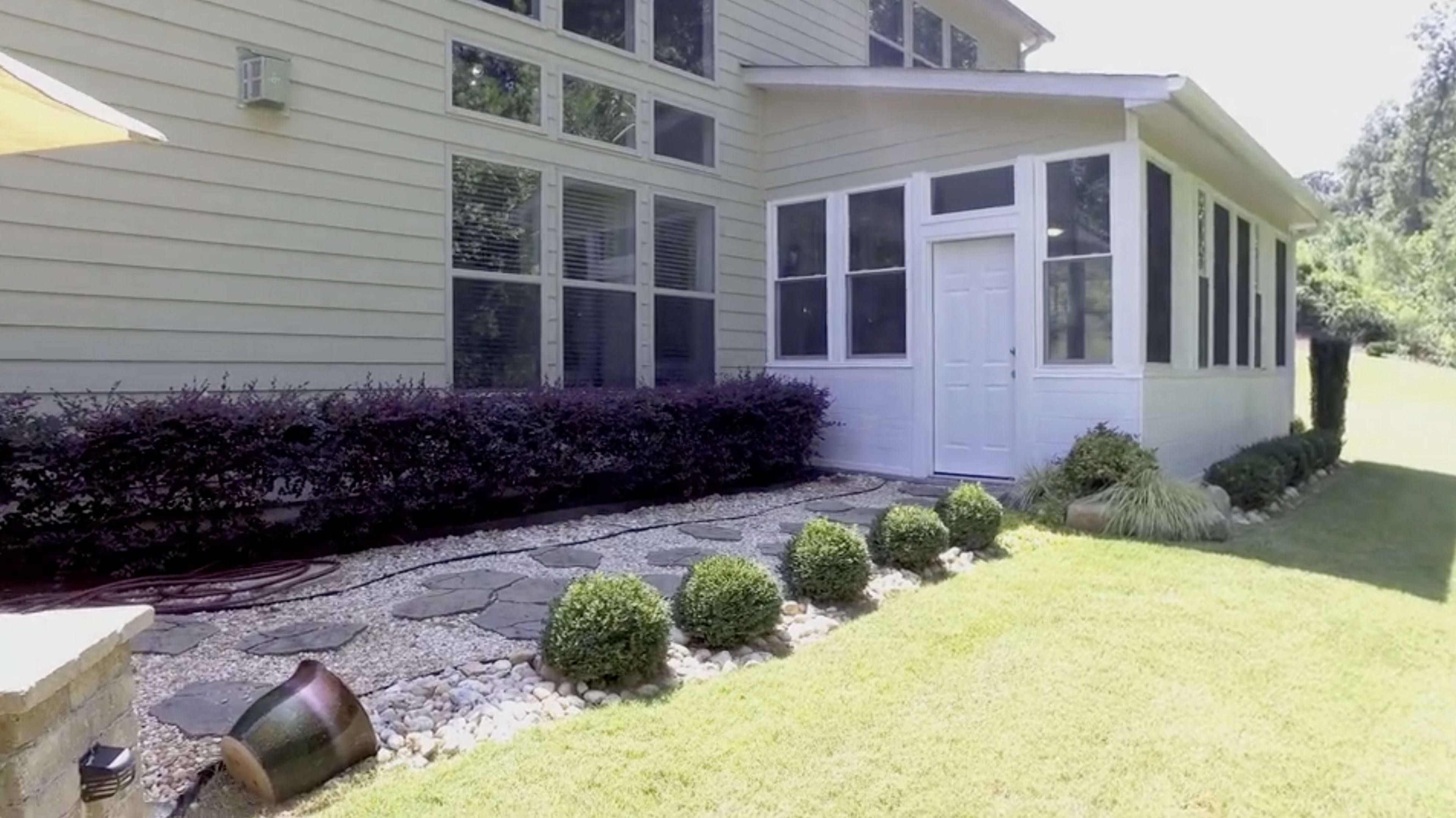A house exterior featuring a stone pathway, a manicured lawn, neatly trimmed bushes, and a white door leading into a sunroom.