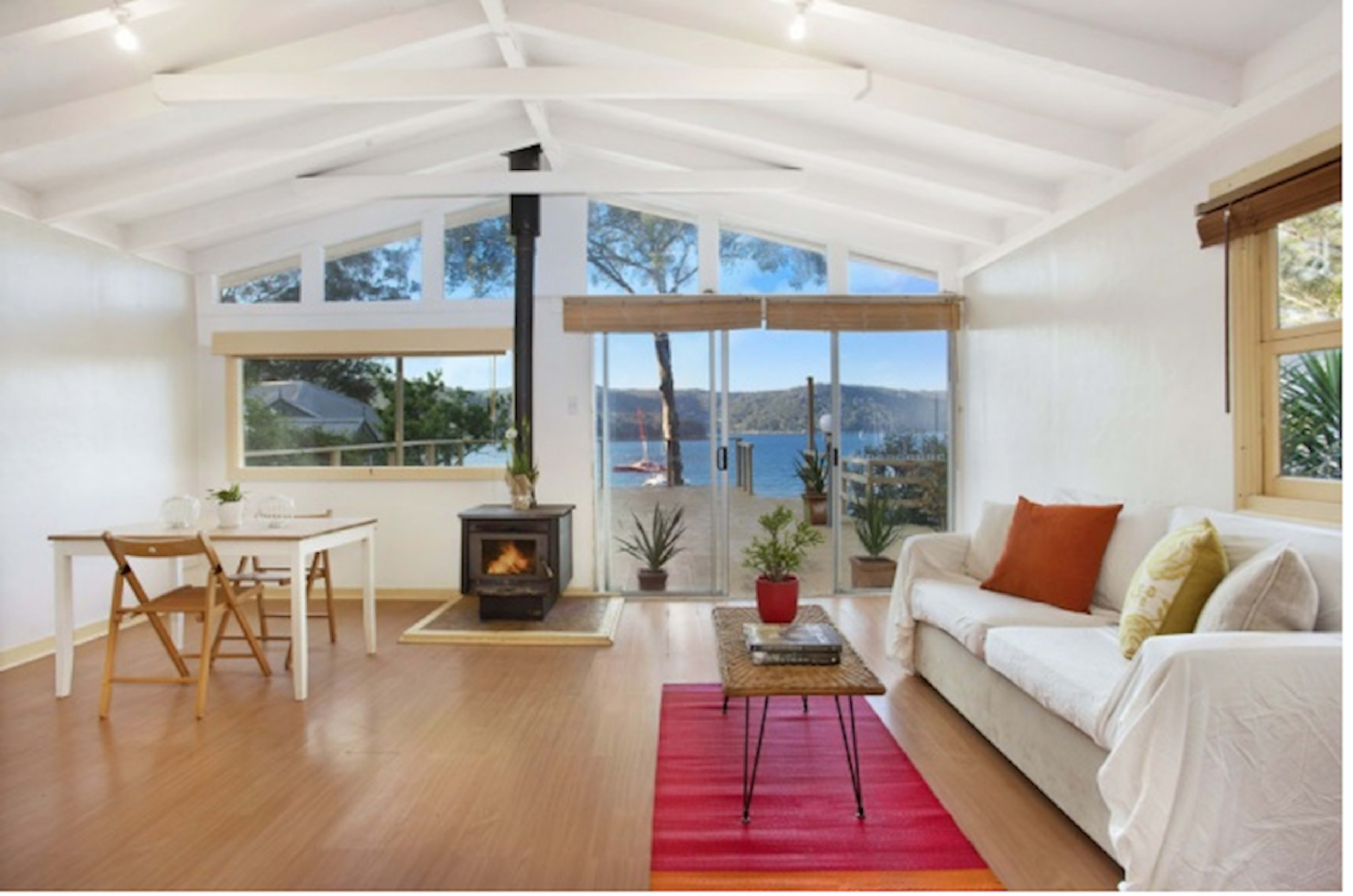 A bright living area with a table and chairs, a fireplace, and large windows overlooking a lake.