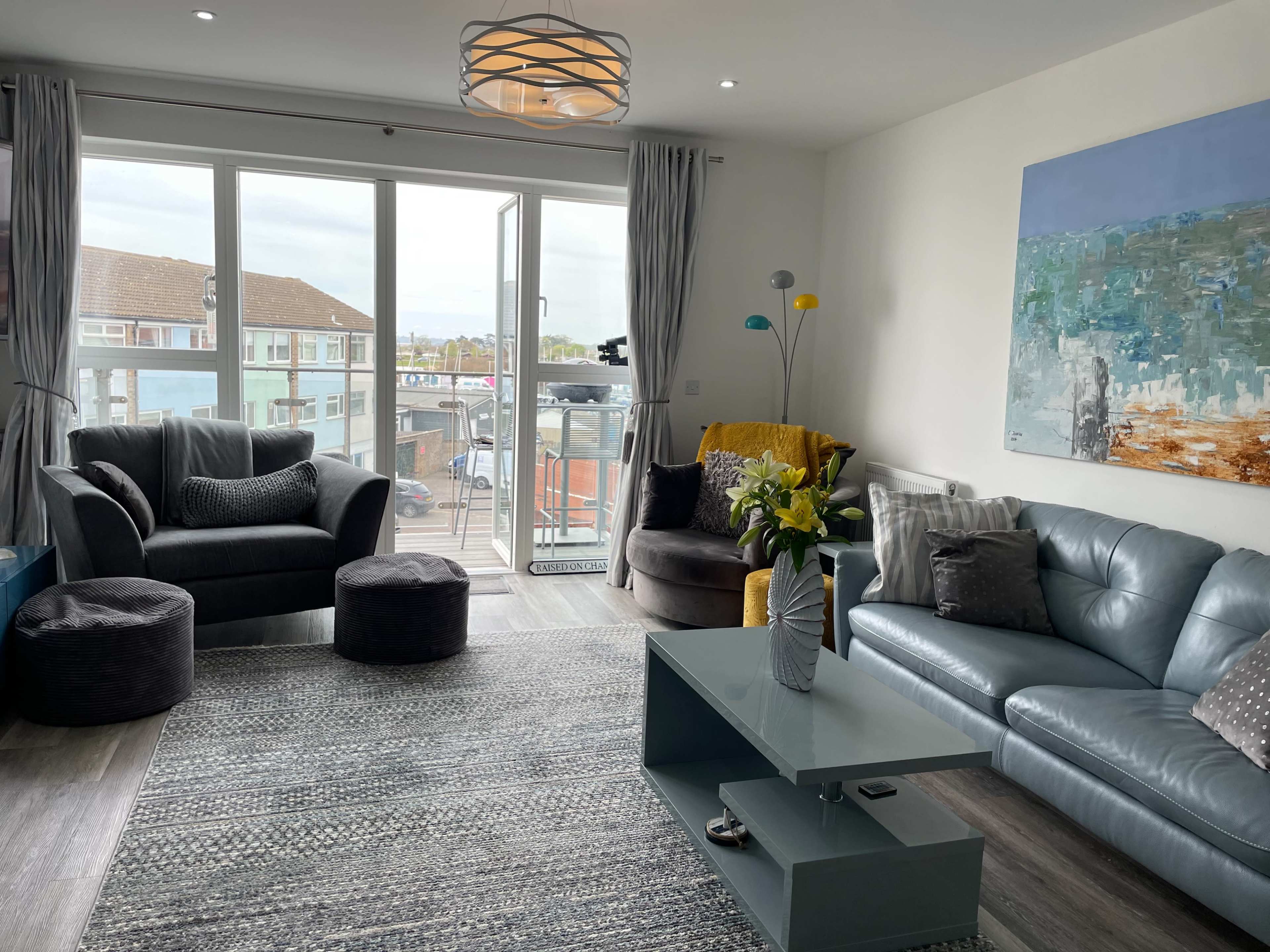 The living room features a light blue sofa, two armchairs, a coffee table, and a large window with a view of an outdoor balcony.