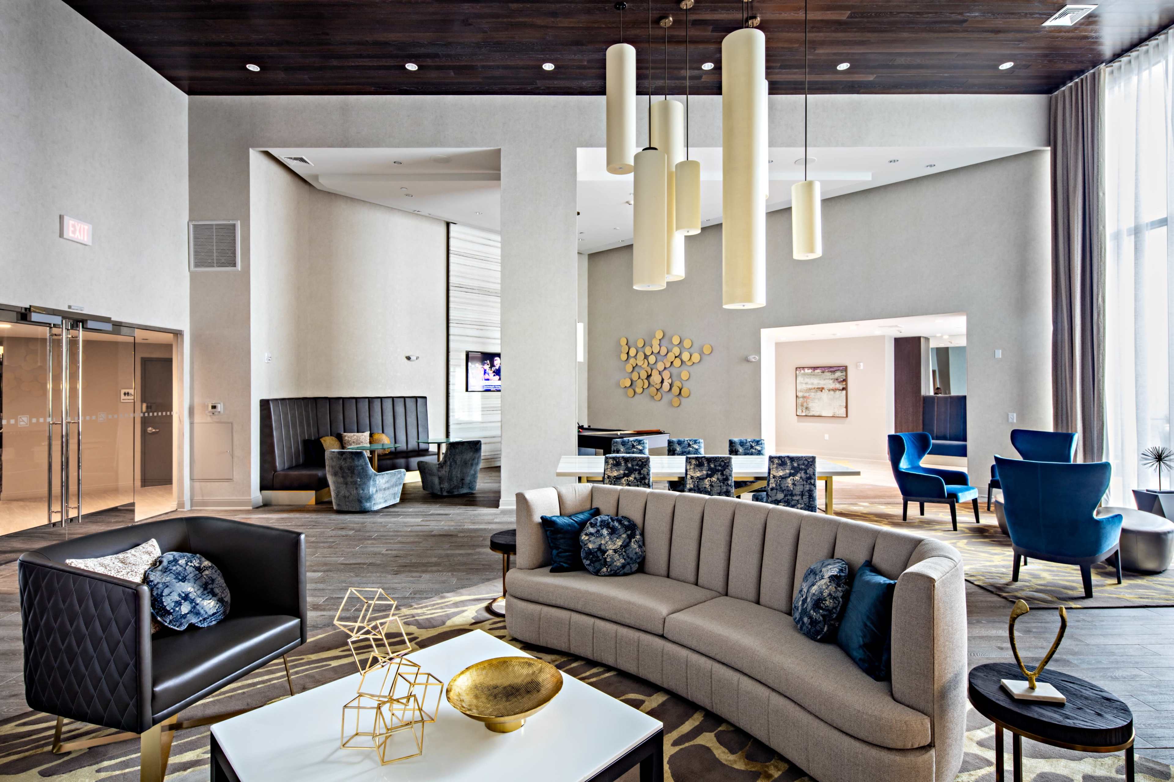A modern lounge area with a curved grey sofa, geometric decorations, and various seating arrangements under pendant lighting.