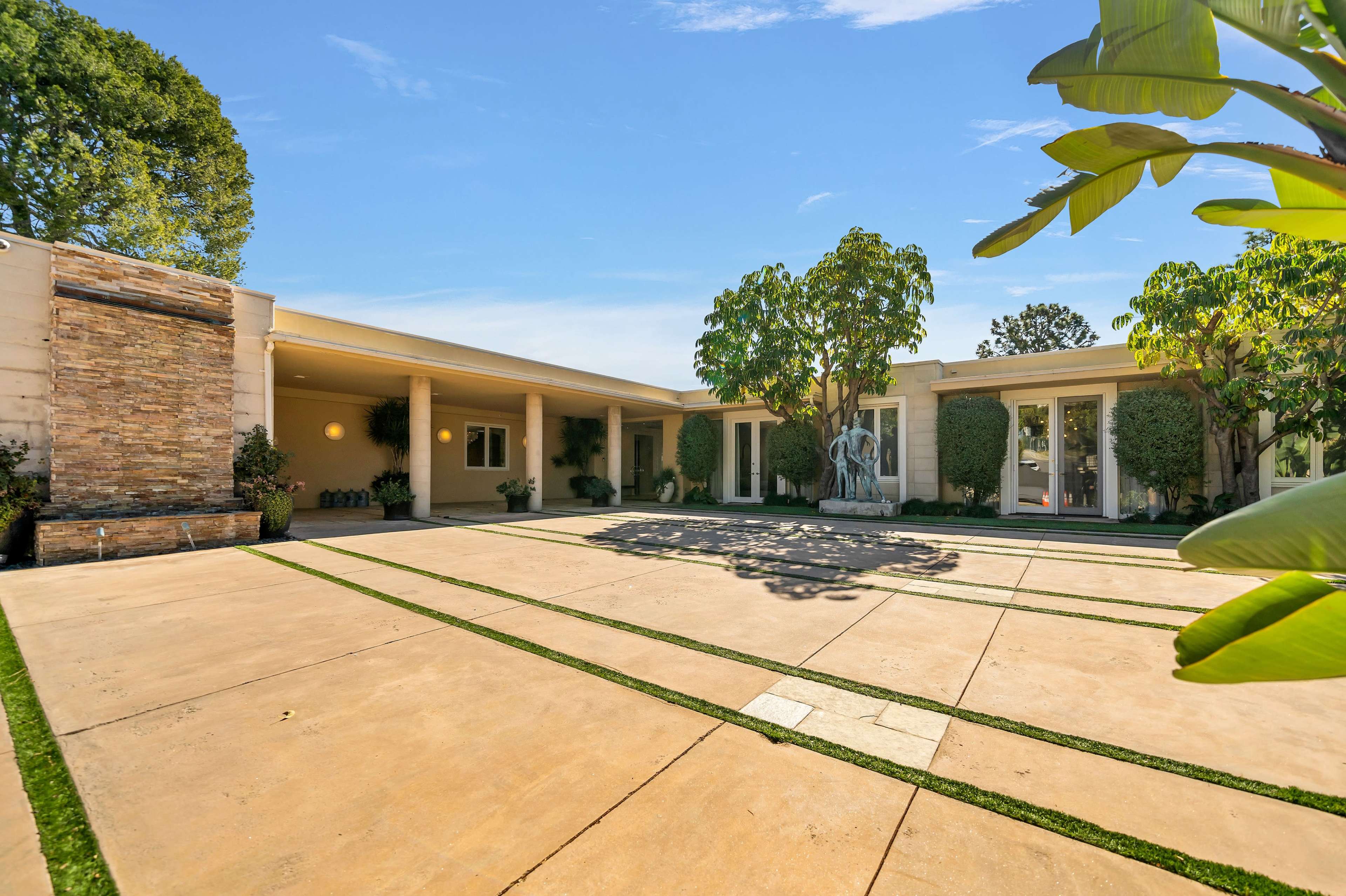 A modern house with a landscaped courtyard featuring stone accents, greenery, and a sculpture.
