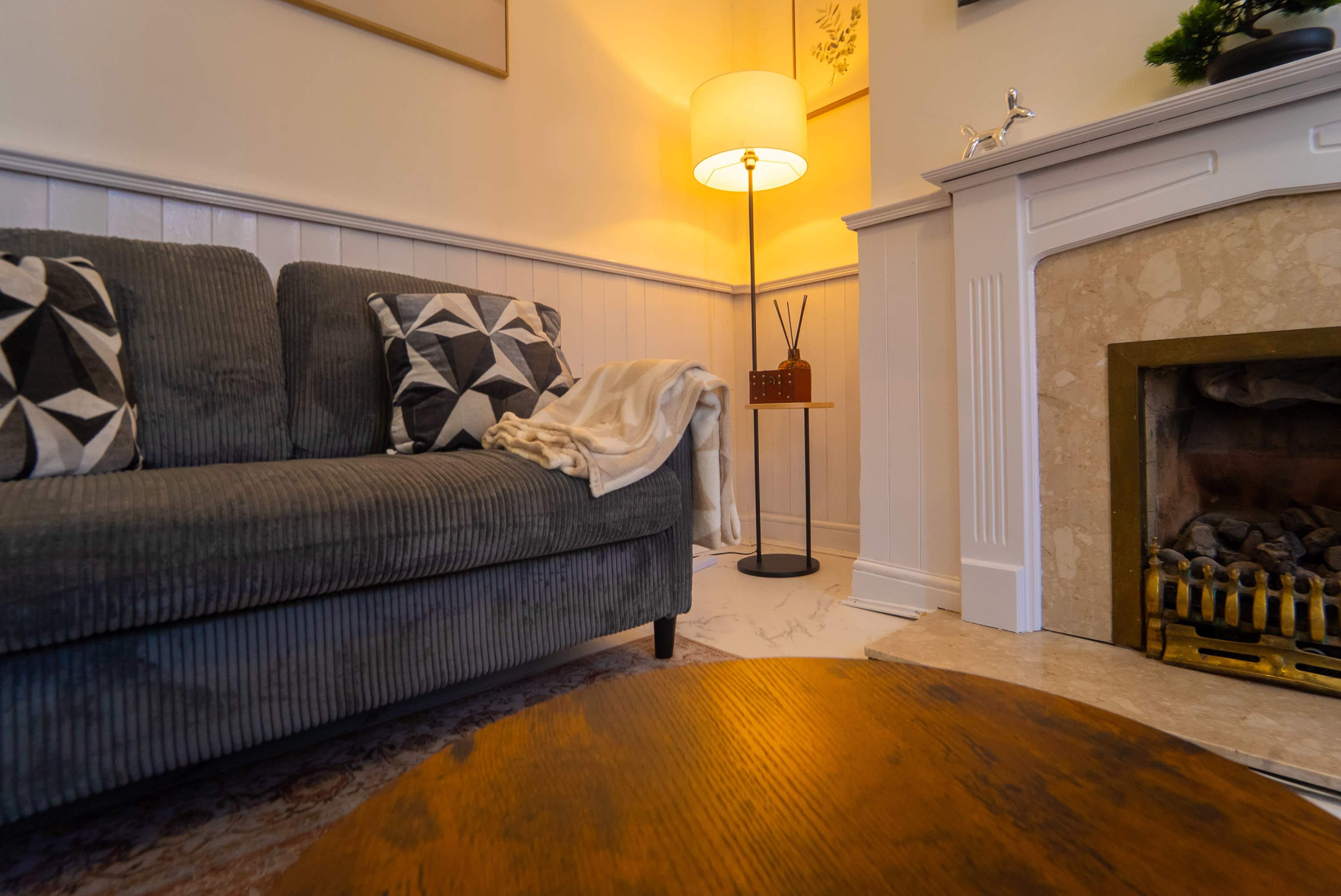 The image depicts a cozy living room with a striped couch, a floor lamp, and a marble fireplace.