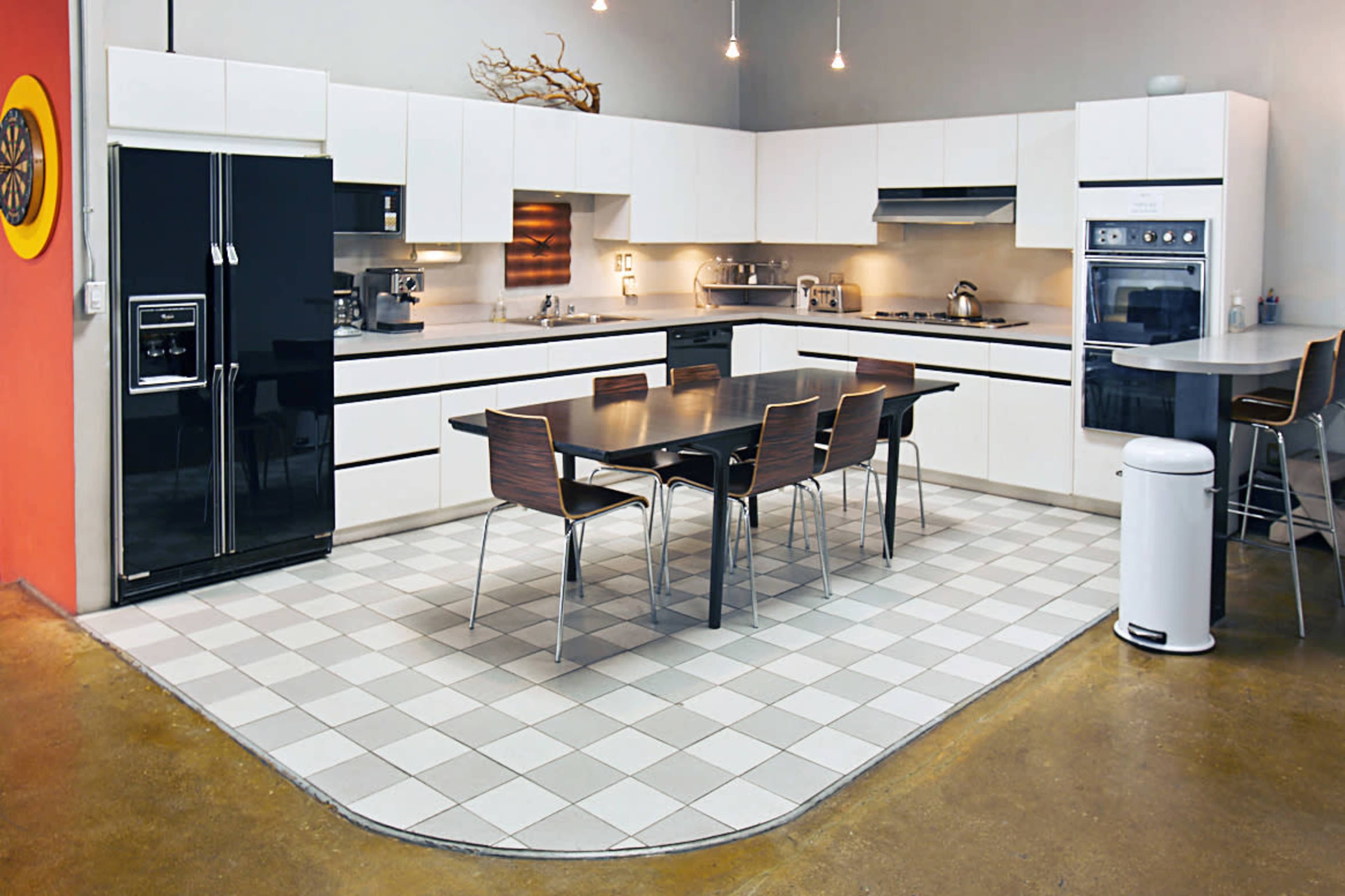 A modern kitchen featuring a large table with chairs, sleek black and white cabinetry, and stainless steel appliances.