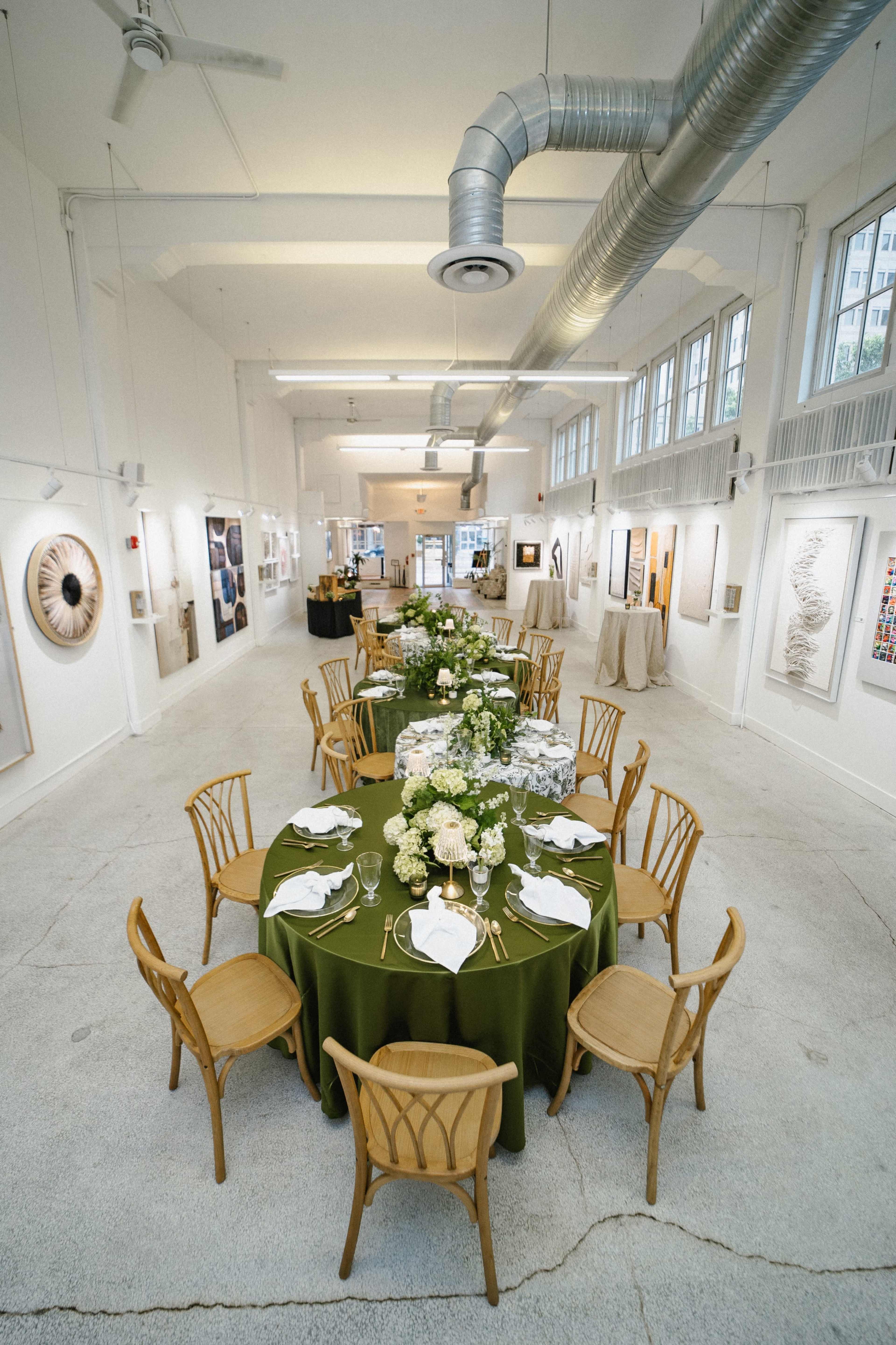 A spacious gallery displays an elegant dining setup with a green tablecloth, white china, and a floral centerpiece, surrounded by wooden chairs.