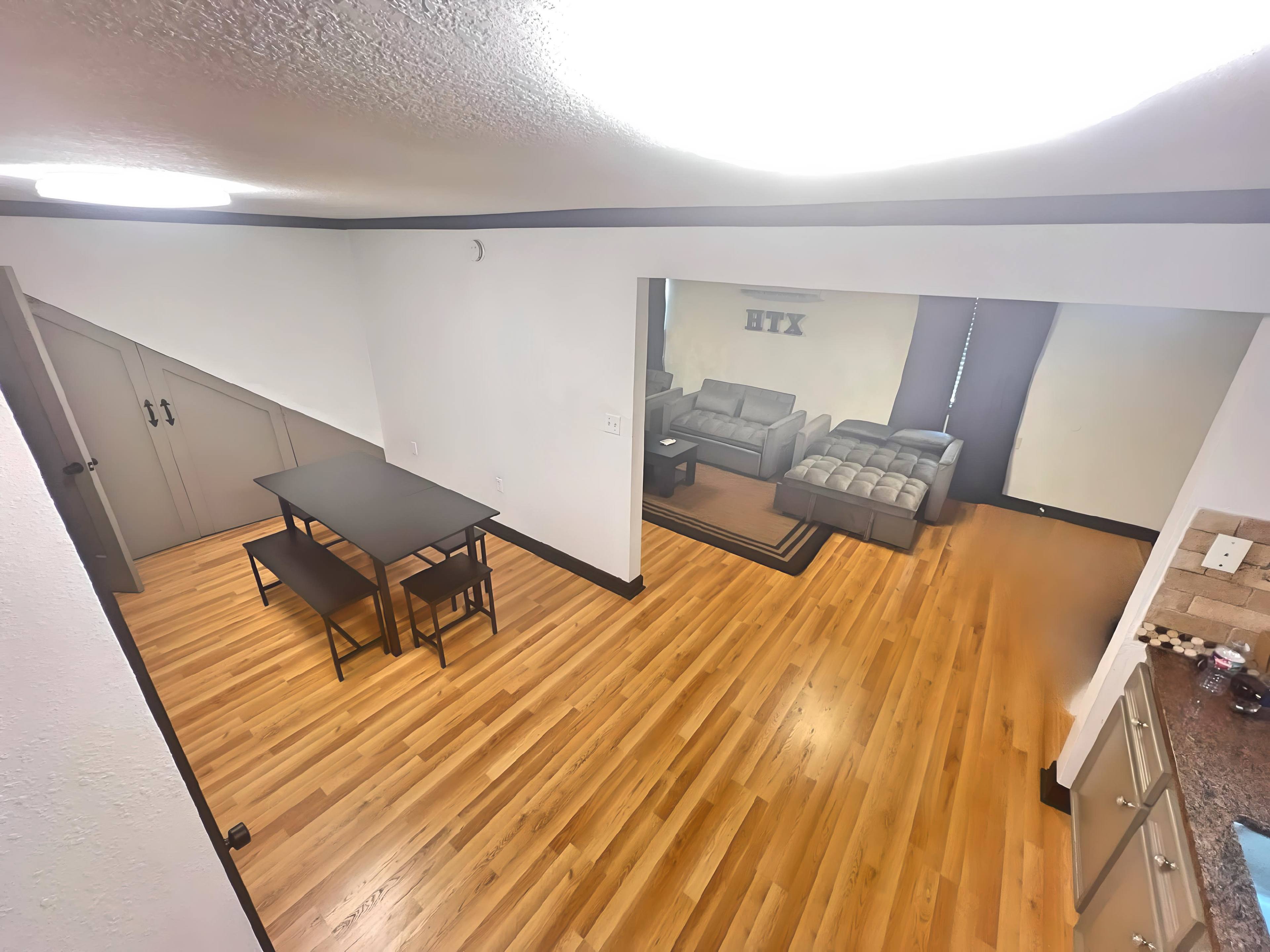 The image shows a spacious open living area with a dining table and chairs, leading to a living room furnished with a sectional couch.