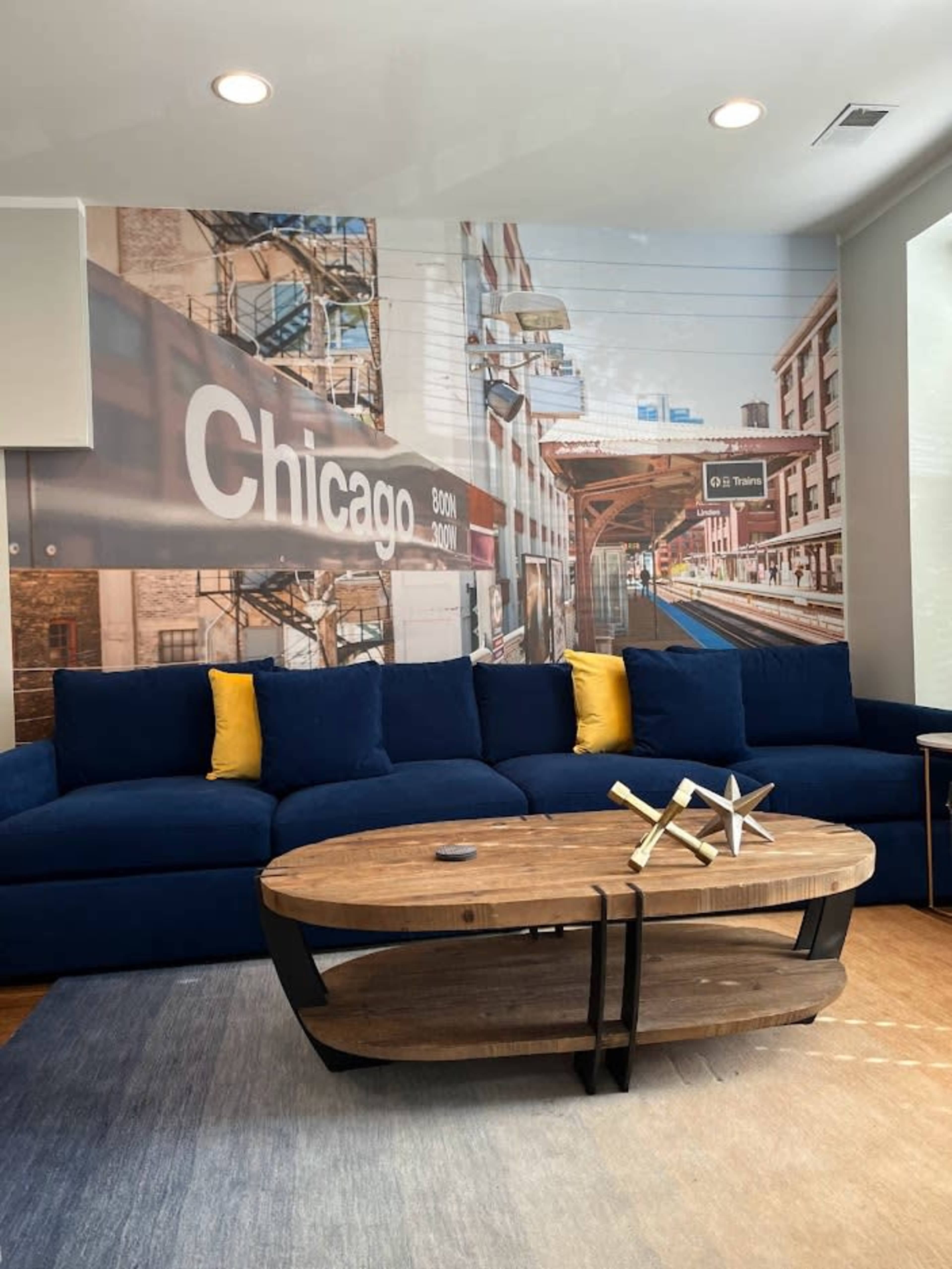 A living room with a blue sectional sofa, a wooden coffee table, and a mural of a Chicago train station on the wall behind it.