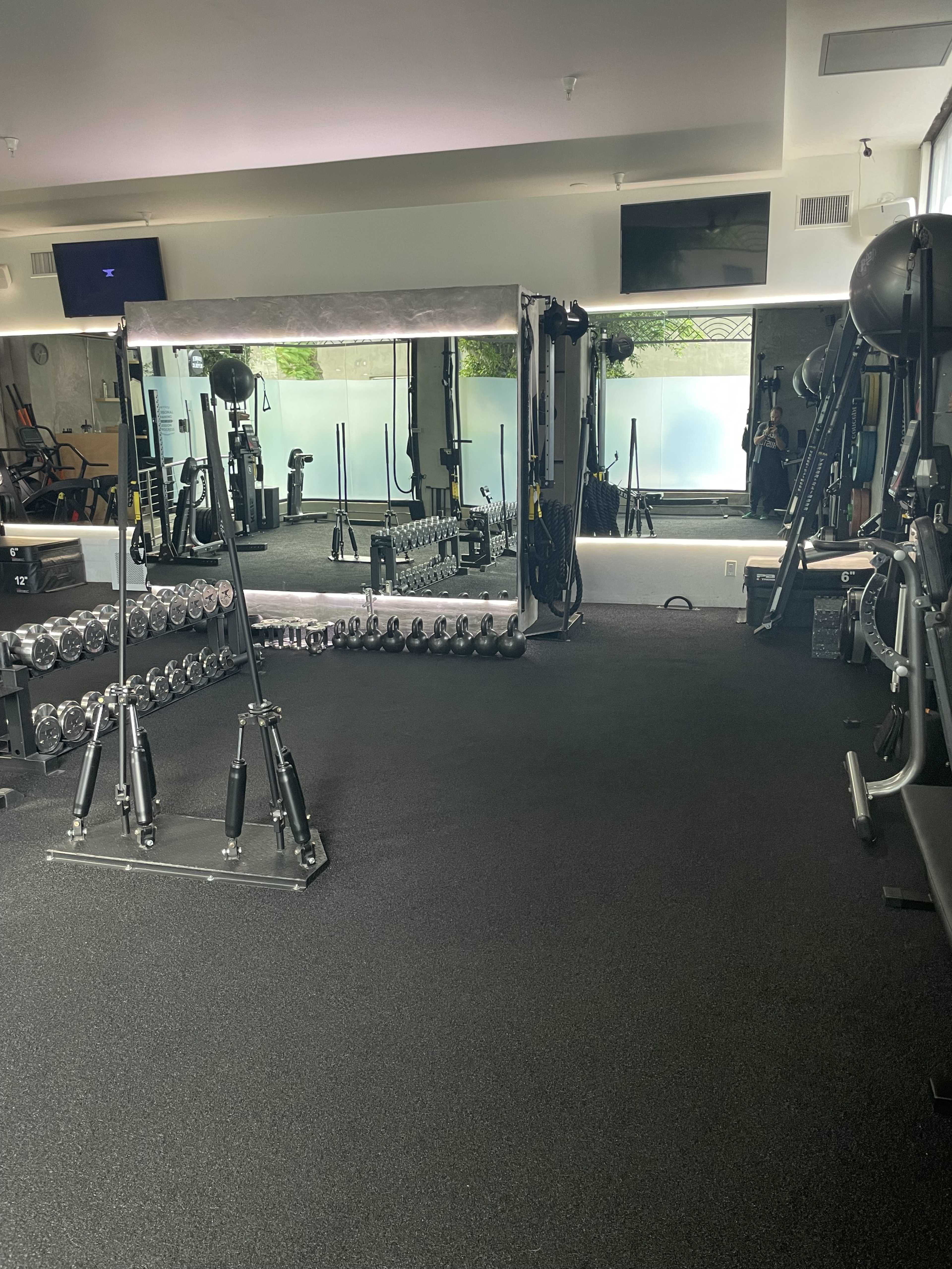A fitness studio with various gym equipment, including dumbbells arranged in a rack and a large mirror across from a workout area.