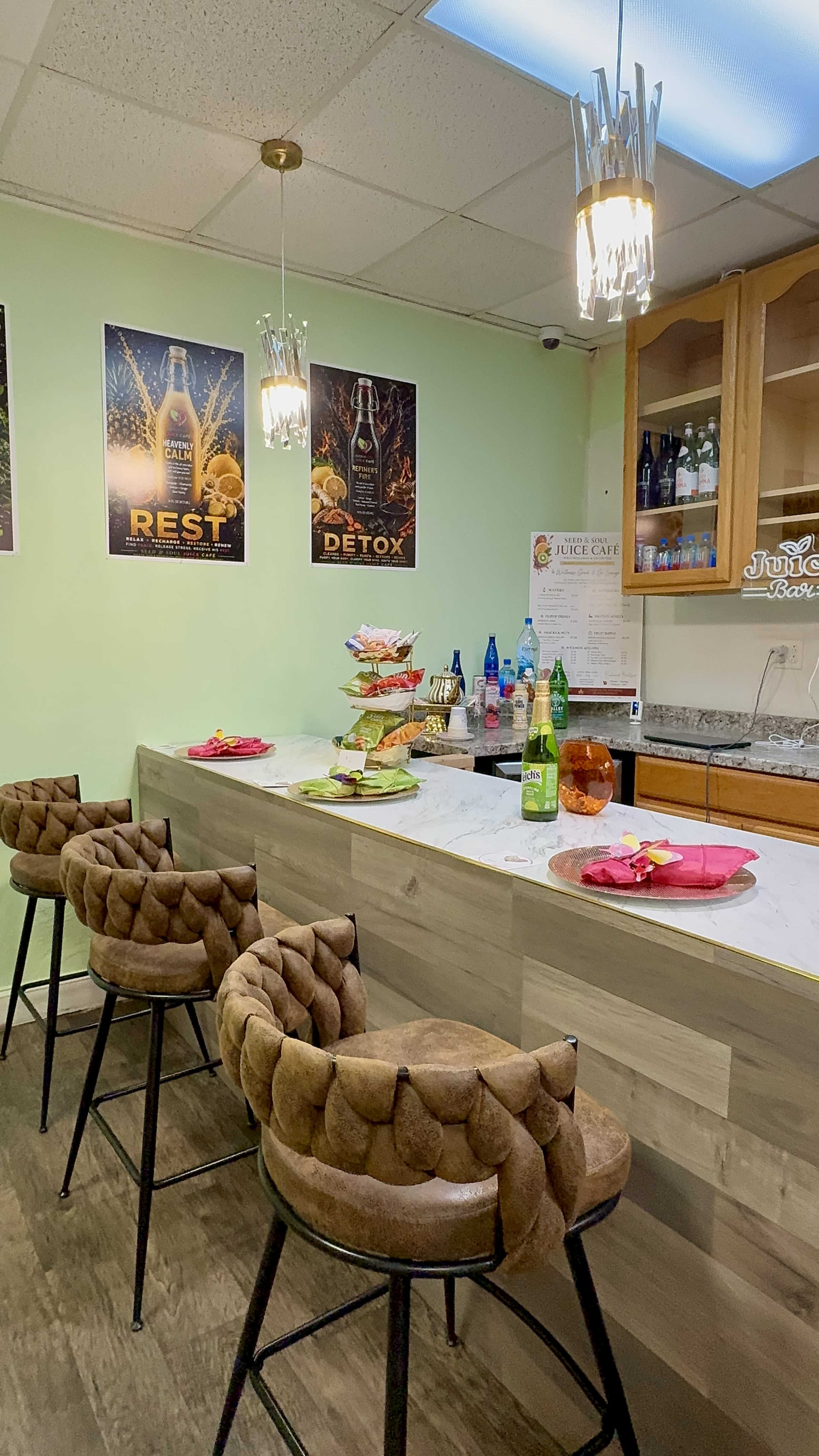 The image shows a cozy juice bar with a marble countertop, brown cushioned stools, and colorful snacks arranged on the counter, alongside beverage displays and wall posters.