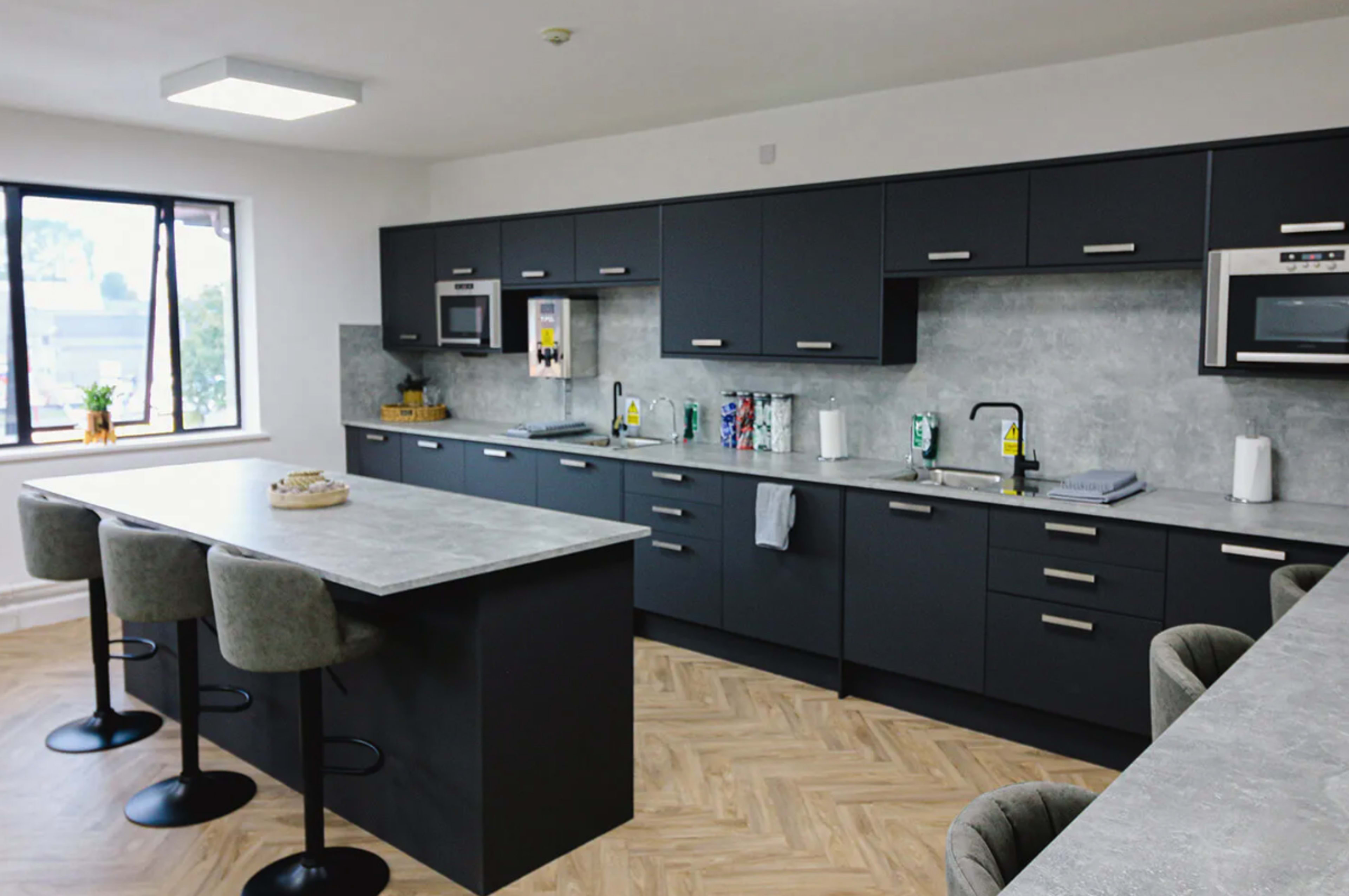 The image shows a modern kitchen with dark cabinetry, a gray countertop, and a central island with bar stools.