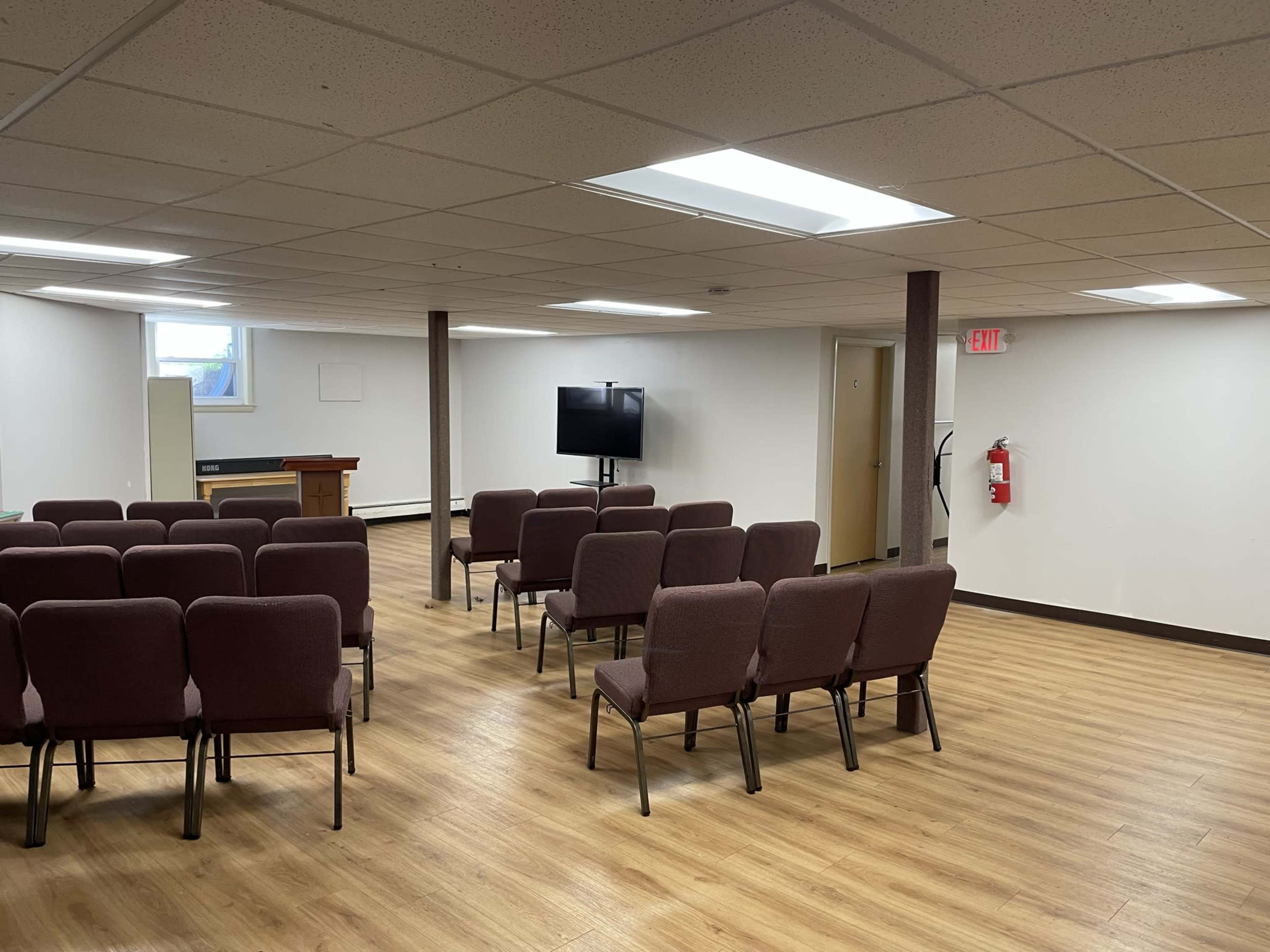 A seating area with several maroon chairs arranged in rows facing a television in a well-lit room with wooden flooring.