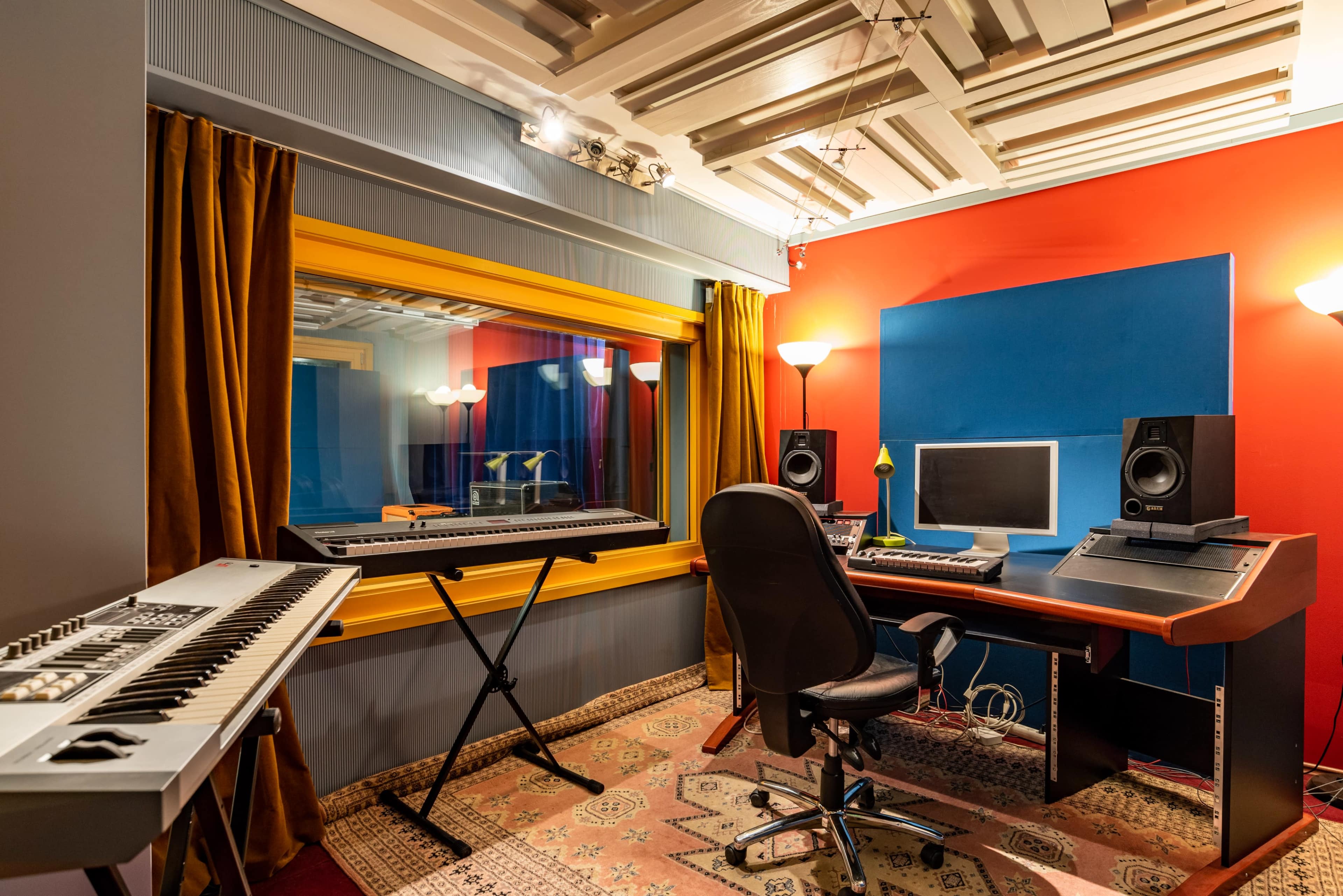 A modern music studio featuring a keyboard, a computer setup, and acoustic panels against colorful walls.