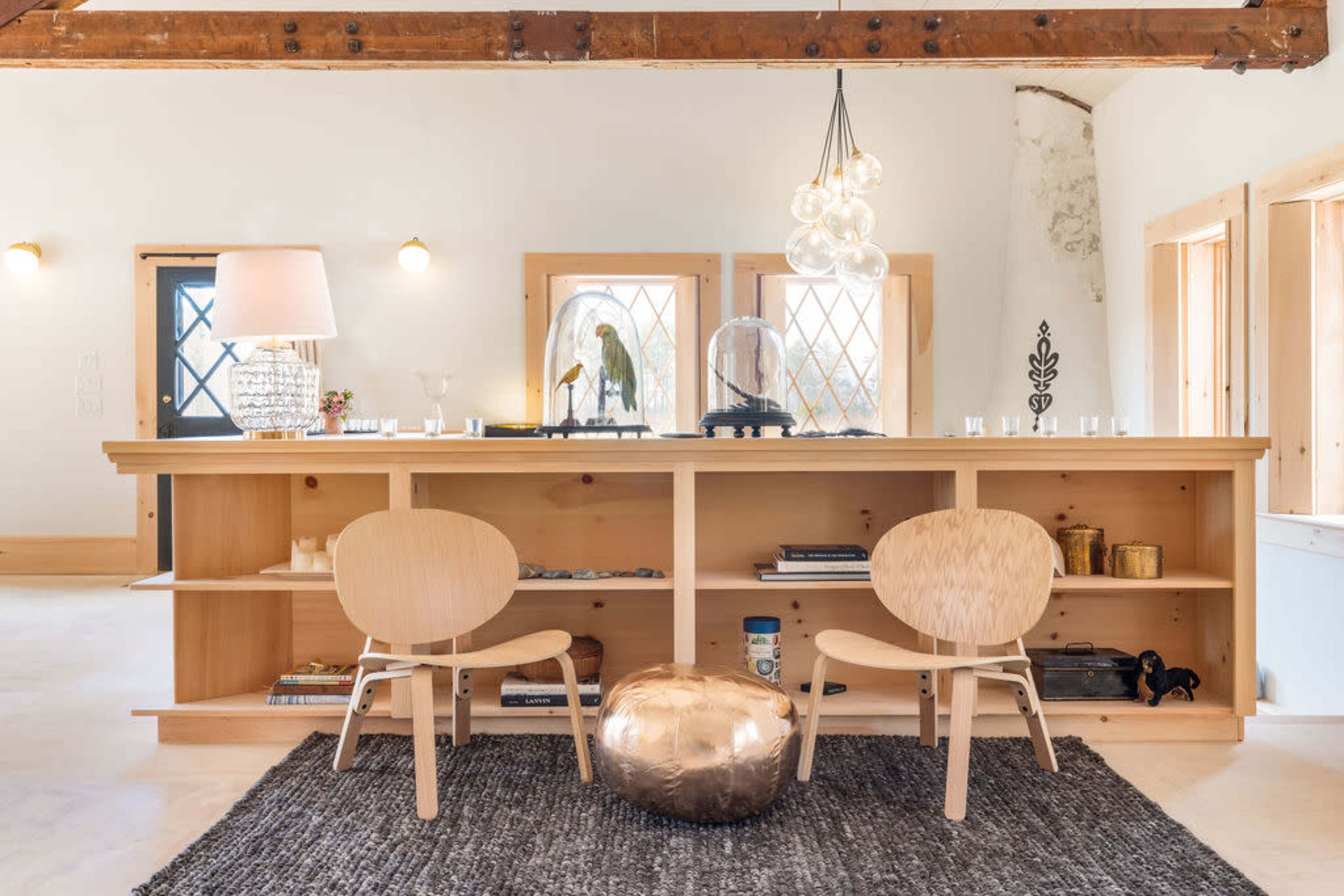 A wooden counter with two chairs and a metallic stool is set against a backdrop of decorative elements and lighting fixtures in a spacious room.