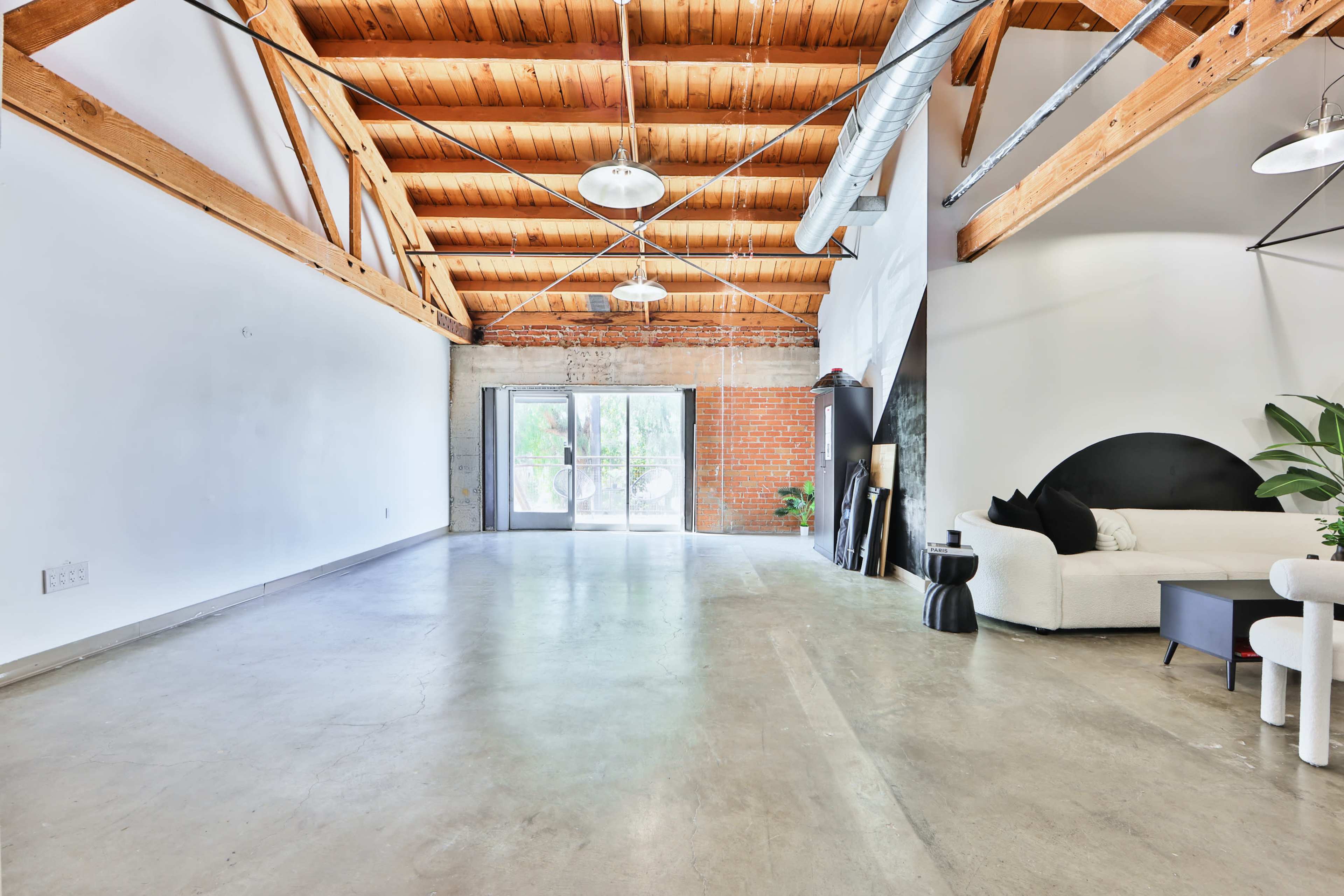 An open interior space with high wooden beams, concrete flooring, and large windows leading to a patio.