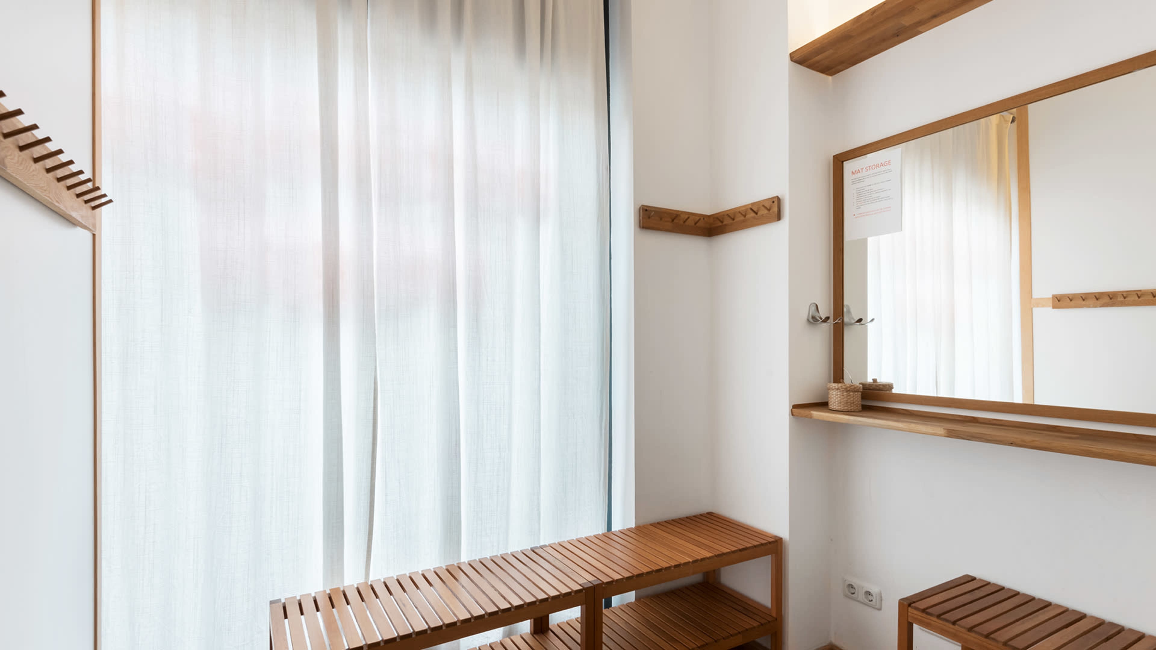 The image shows a minimalist indoor space featuring a mirror, a wooden bench, and a light curtain.