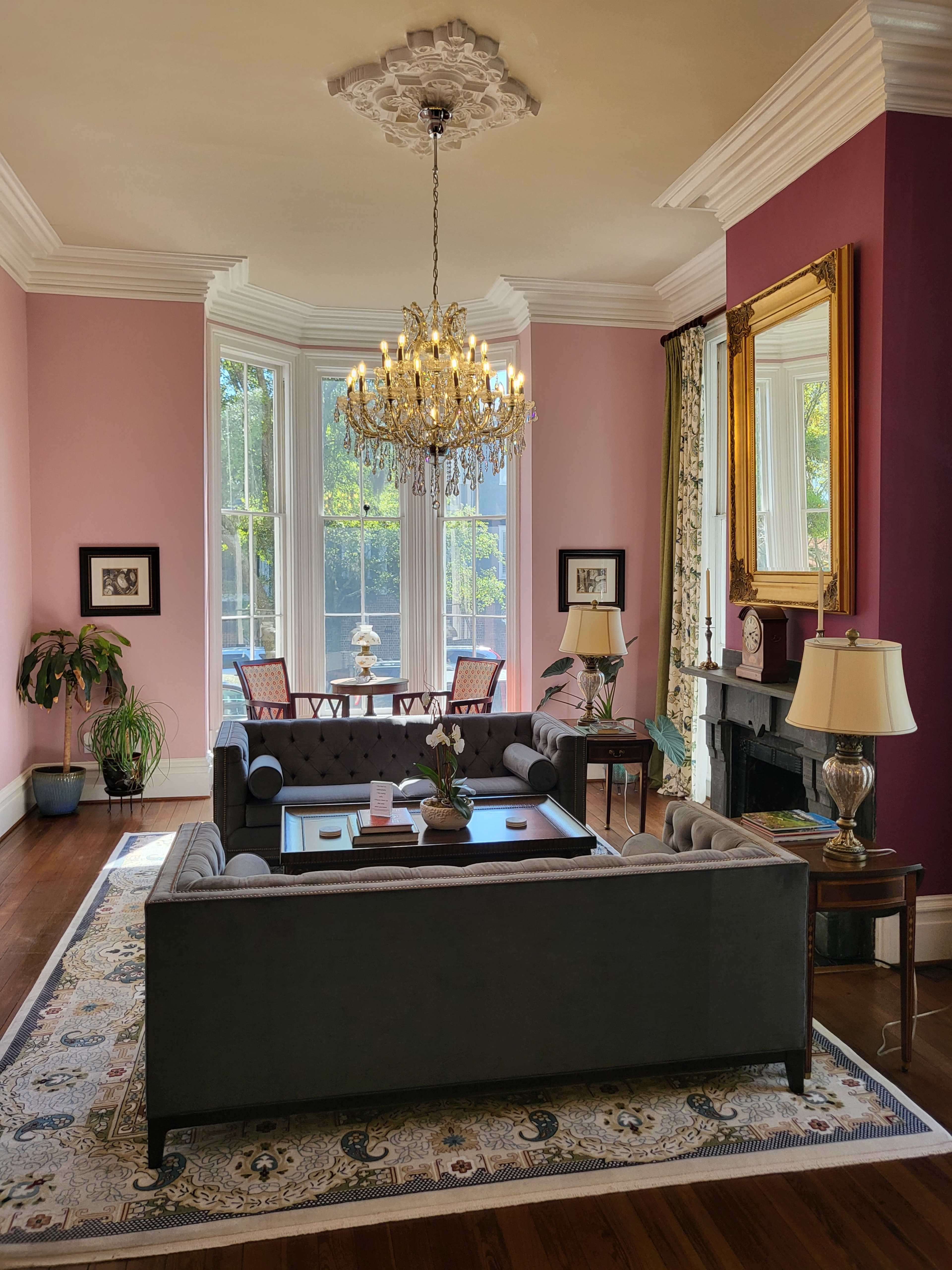 A living room with a chandelier, a gray sofa set, a coffee table, and a dining area visible through large windows.