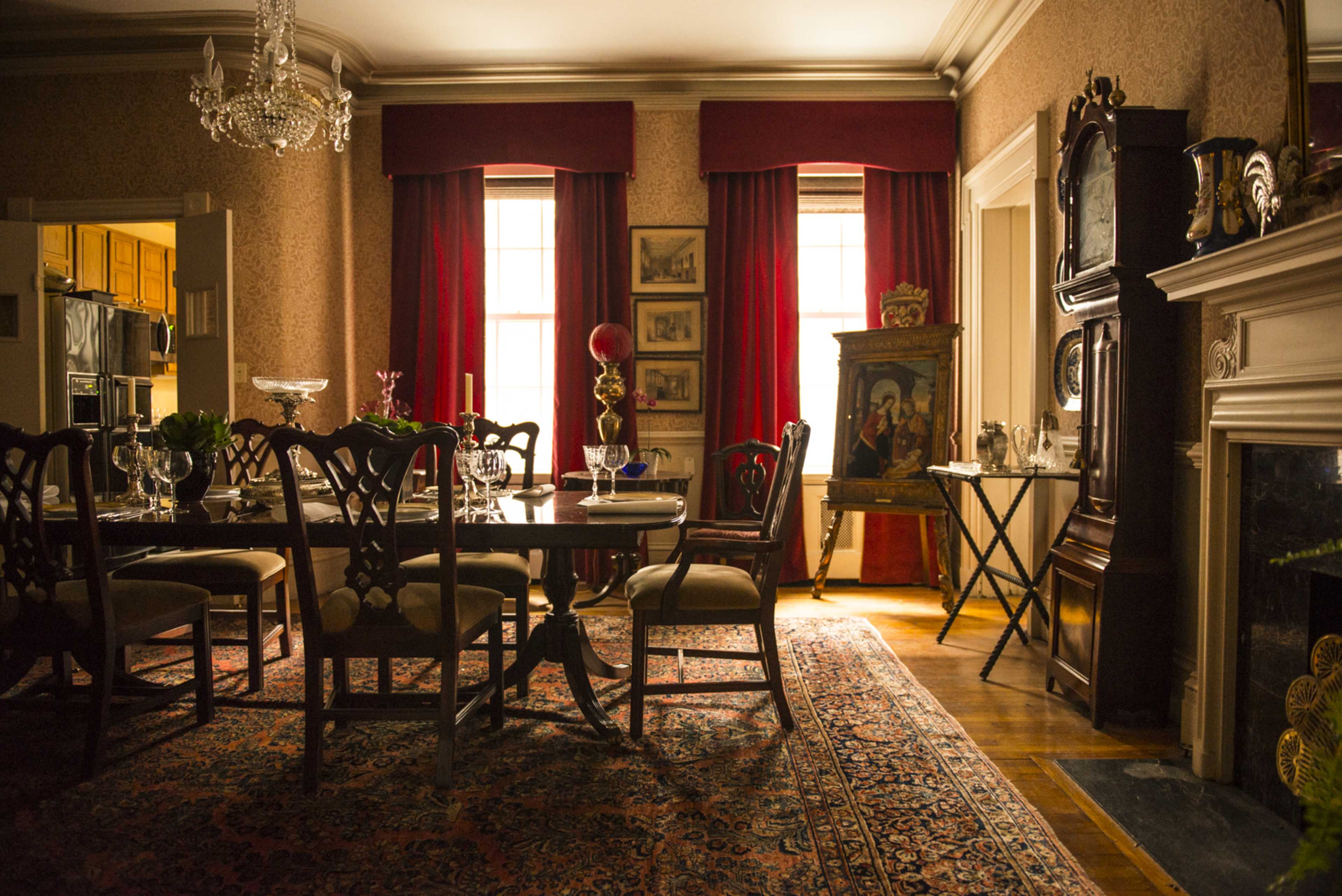 An elegantly furnished dining room with a large table, ornate chairs, and a decorative rug, illuminated by natural light from the windows.