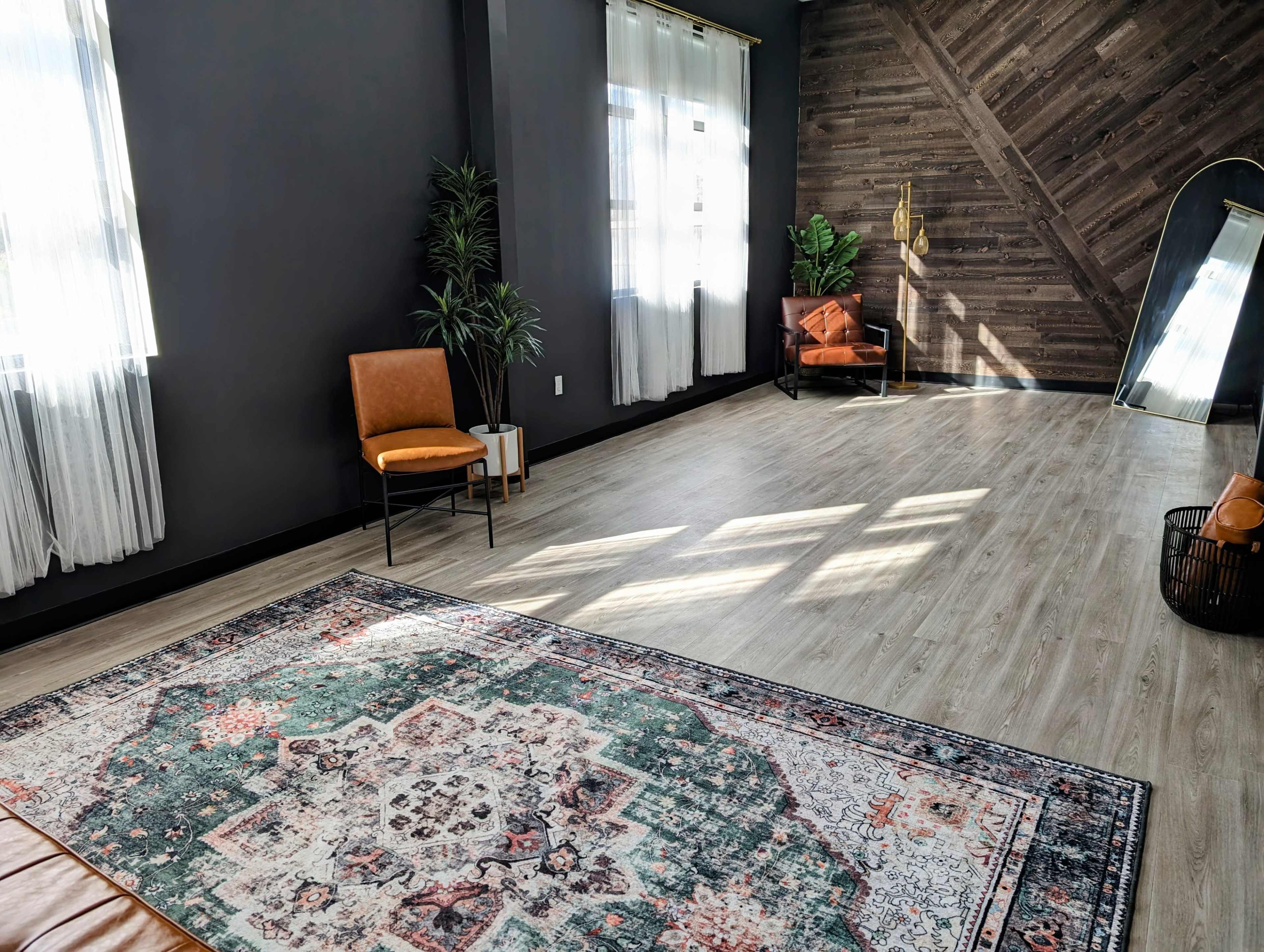 A large, well-lit room with wooden walls, a patterned rug on the floor, and two chairs positioned near a window.