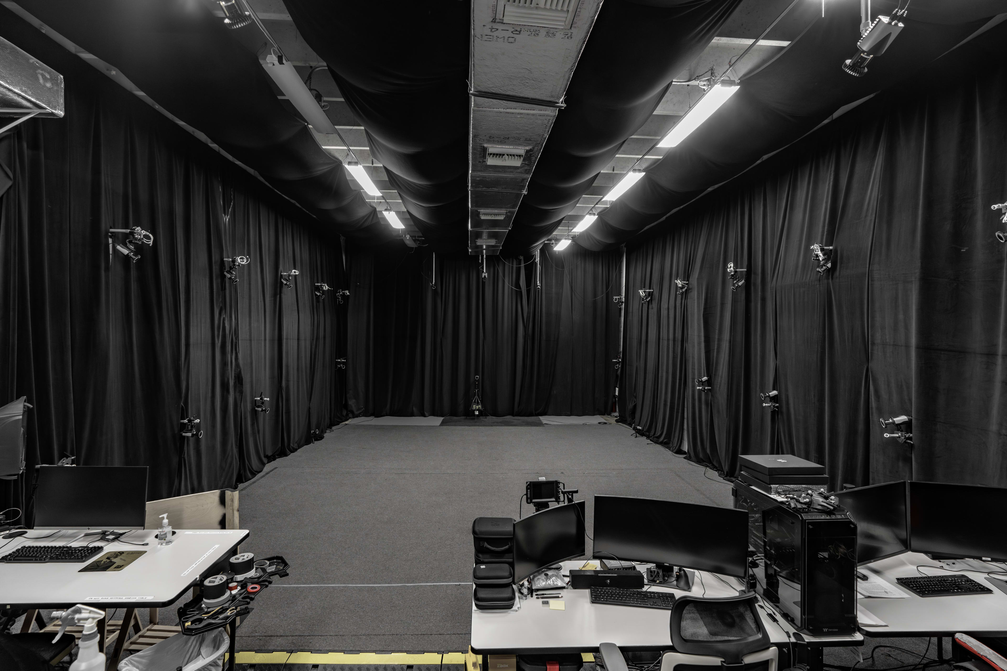A large motion capture studio is shown, with black curtains lining the walls and multiple cameras mounted above an empty performance space.