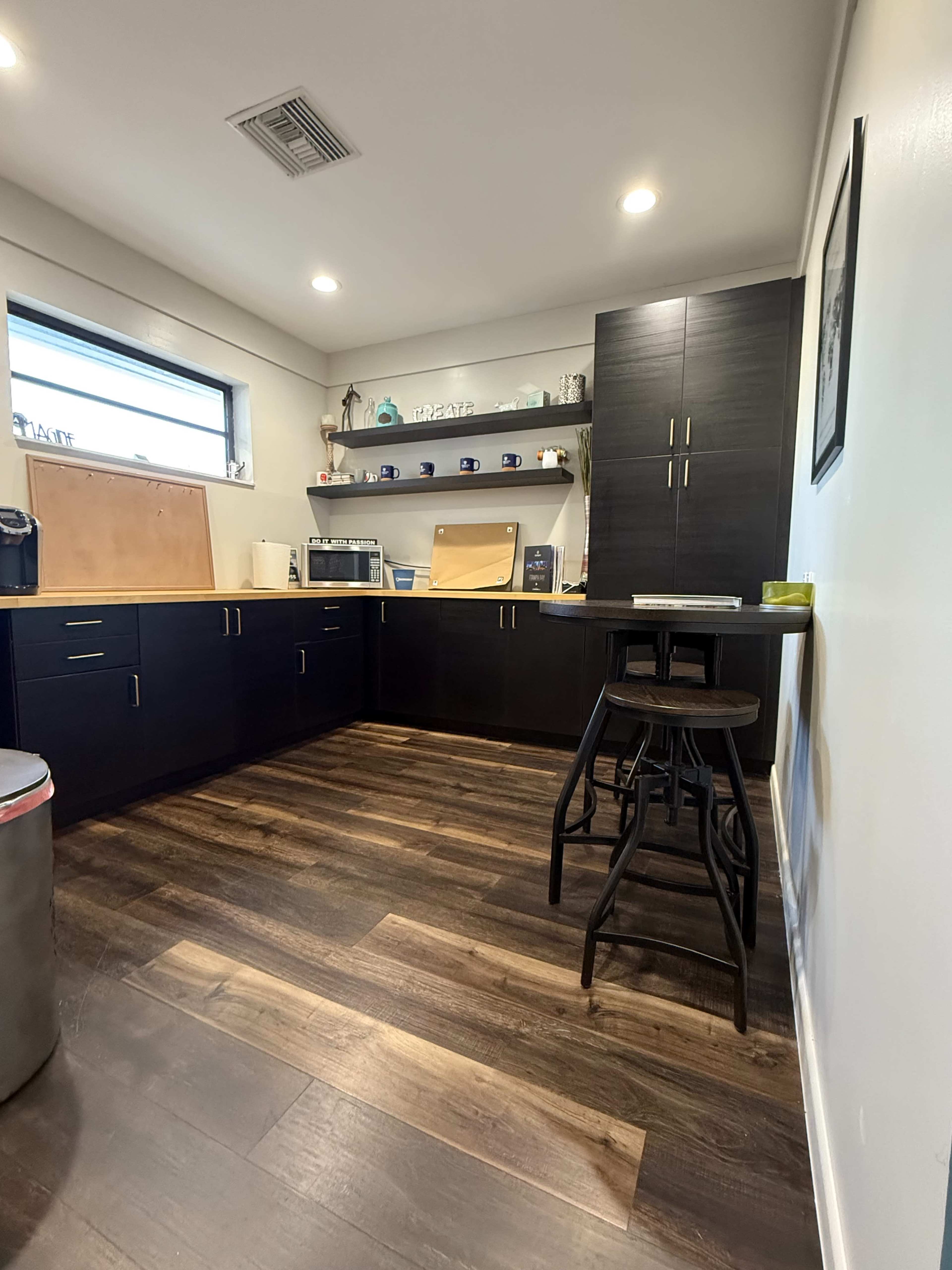 The image shows a modern kitchen with dark cabinetry, a wooden countertop, and a small seating area.