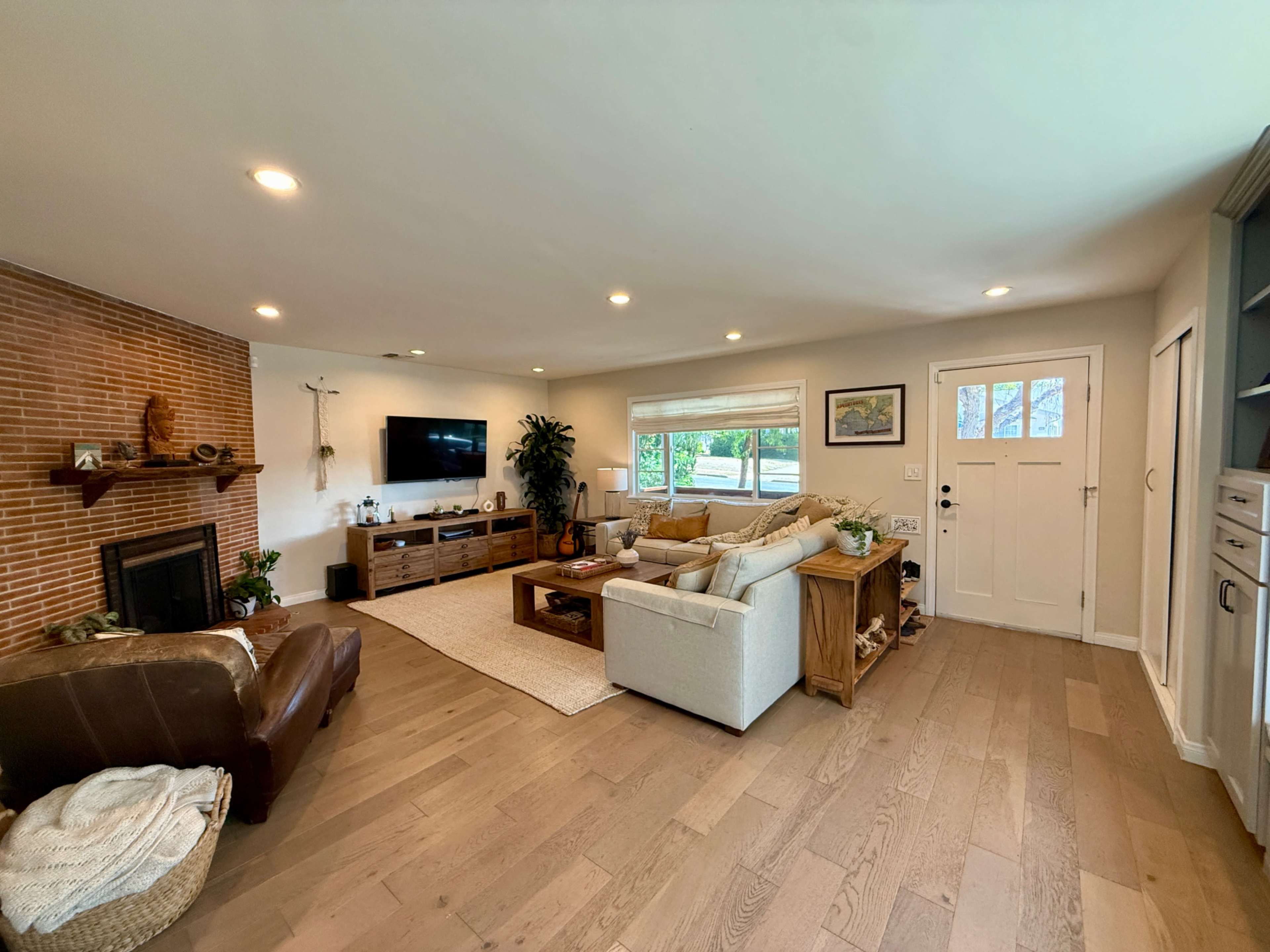 The image shows a spacious living room with a brick fireplace, a comfortable sofa, and a large window, featuring a mixture of modern and cozy decor.