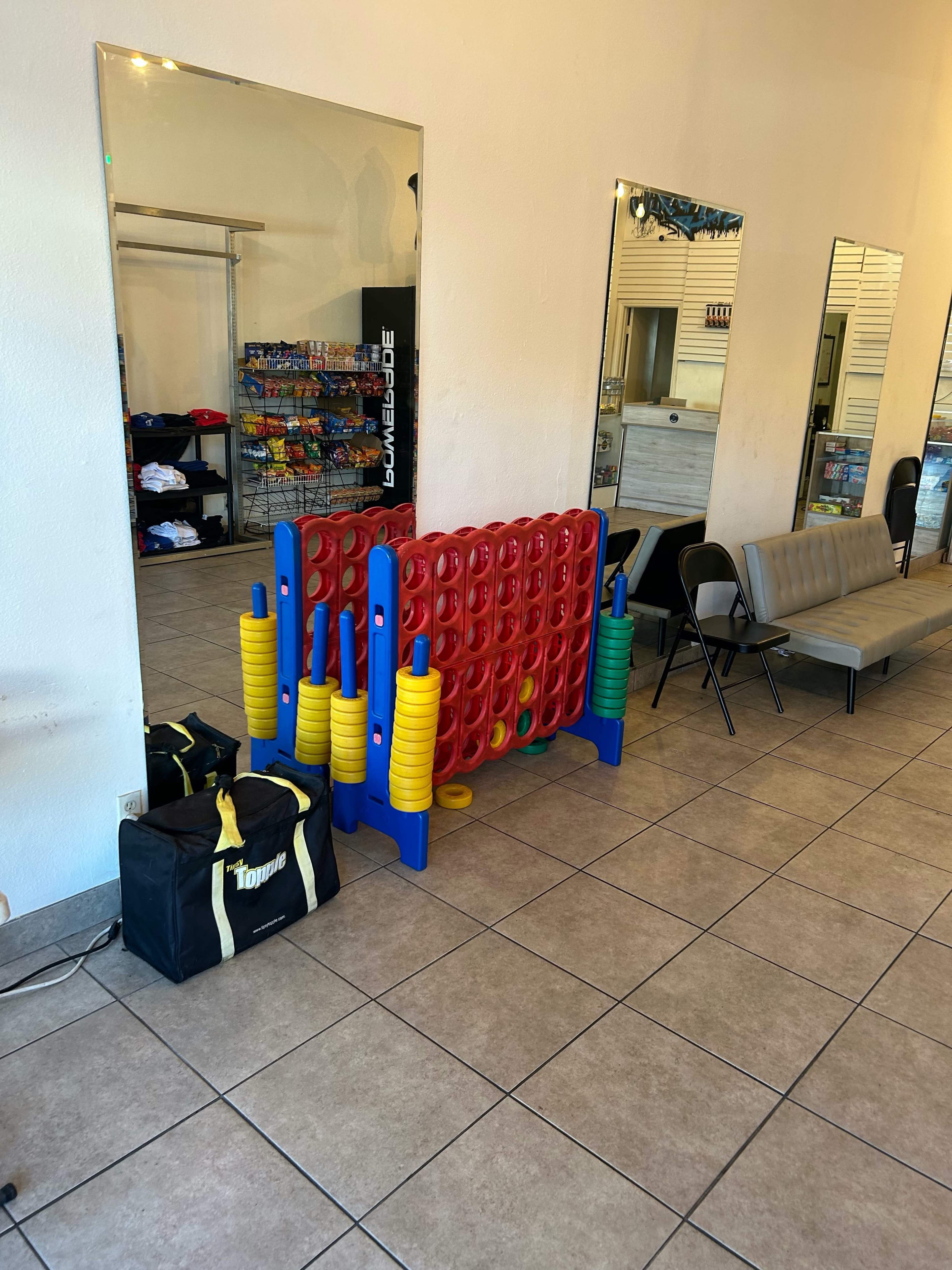 The image shows a colorful weight plate storage rack positioned against a wall in a fitness facility, with mirrors and a seating area visible in the background.