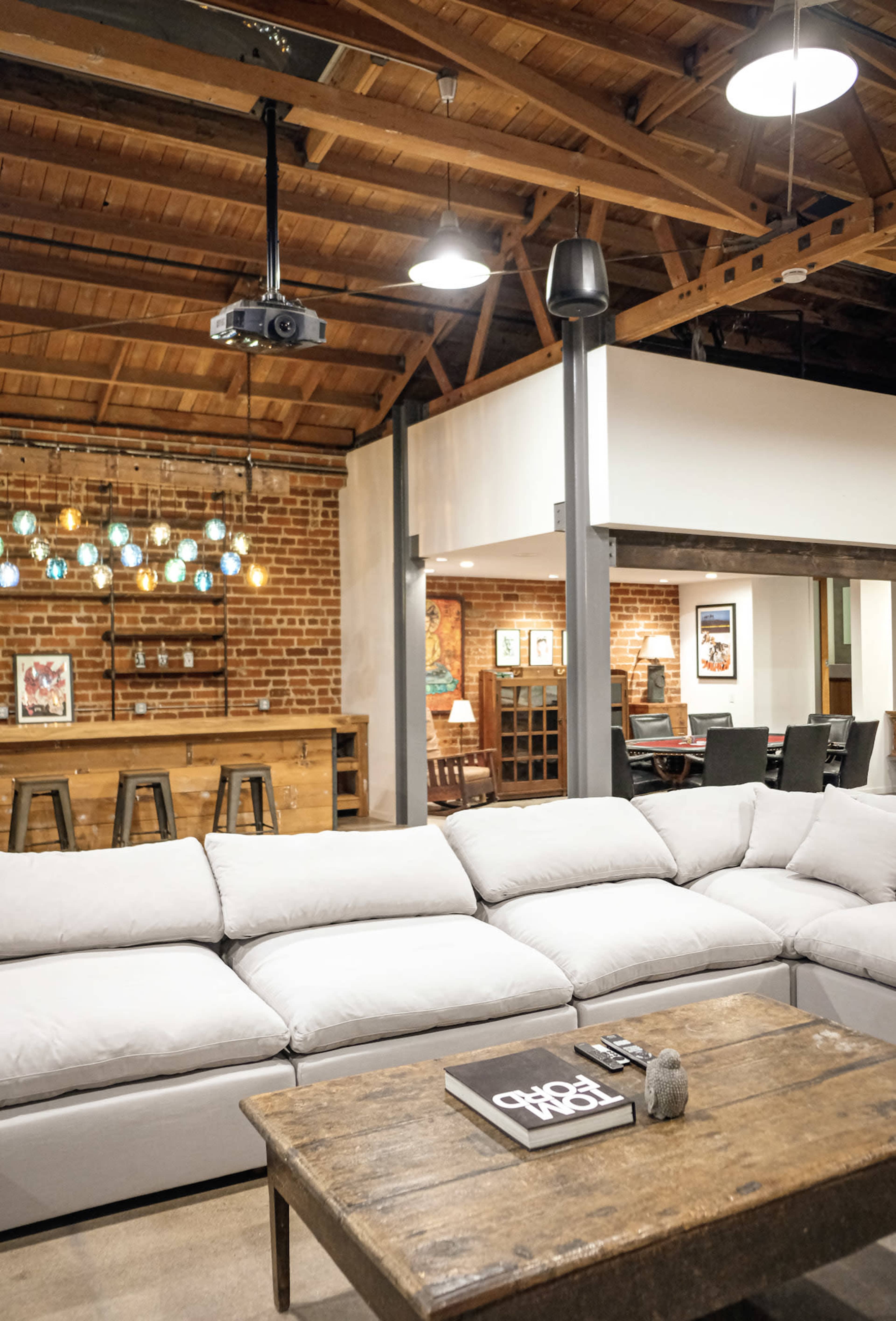 The image shows a spacious living area featuring a large sectional sofa, a wooden coffee table, and a bar with stool seating under pendant lights.