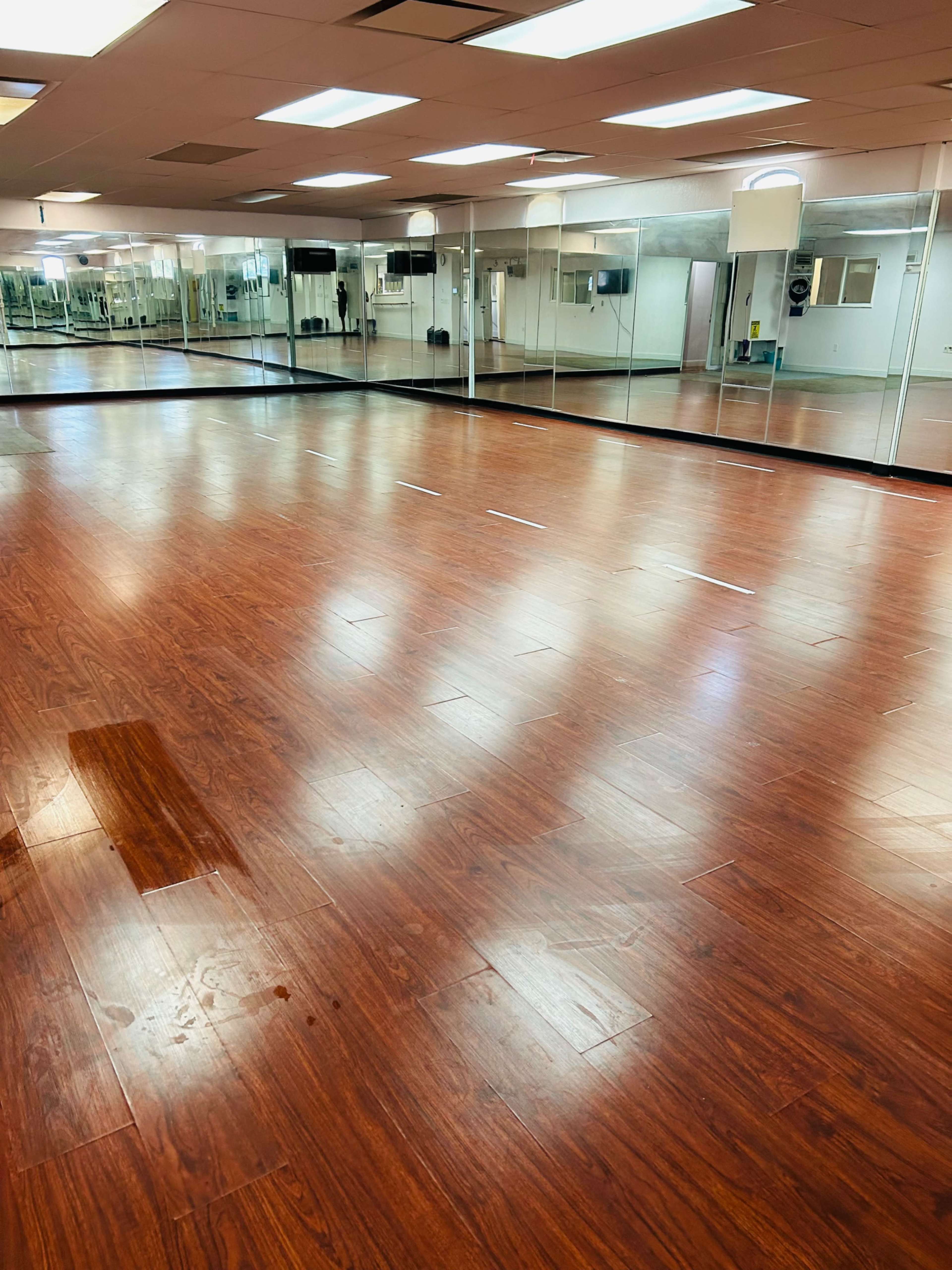 A spacious room with wooden flooring and large mirrors along one wall, typically used for fitness or dance activities.