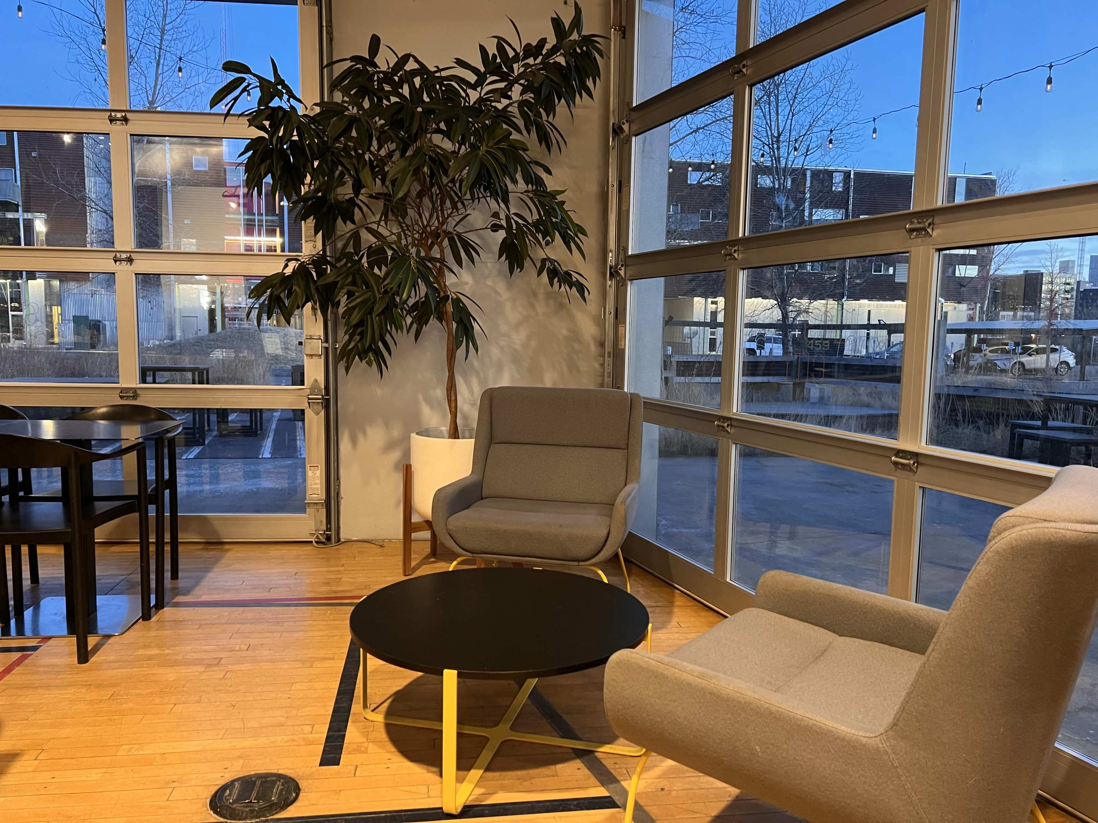 The scene shows a cozy seating area with two gray chairs and a black coffee table beside a large window, revealing a nighttime outdoor view.