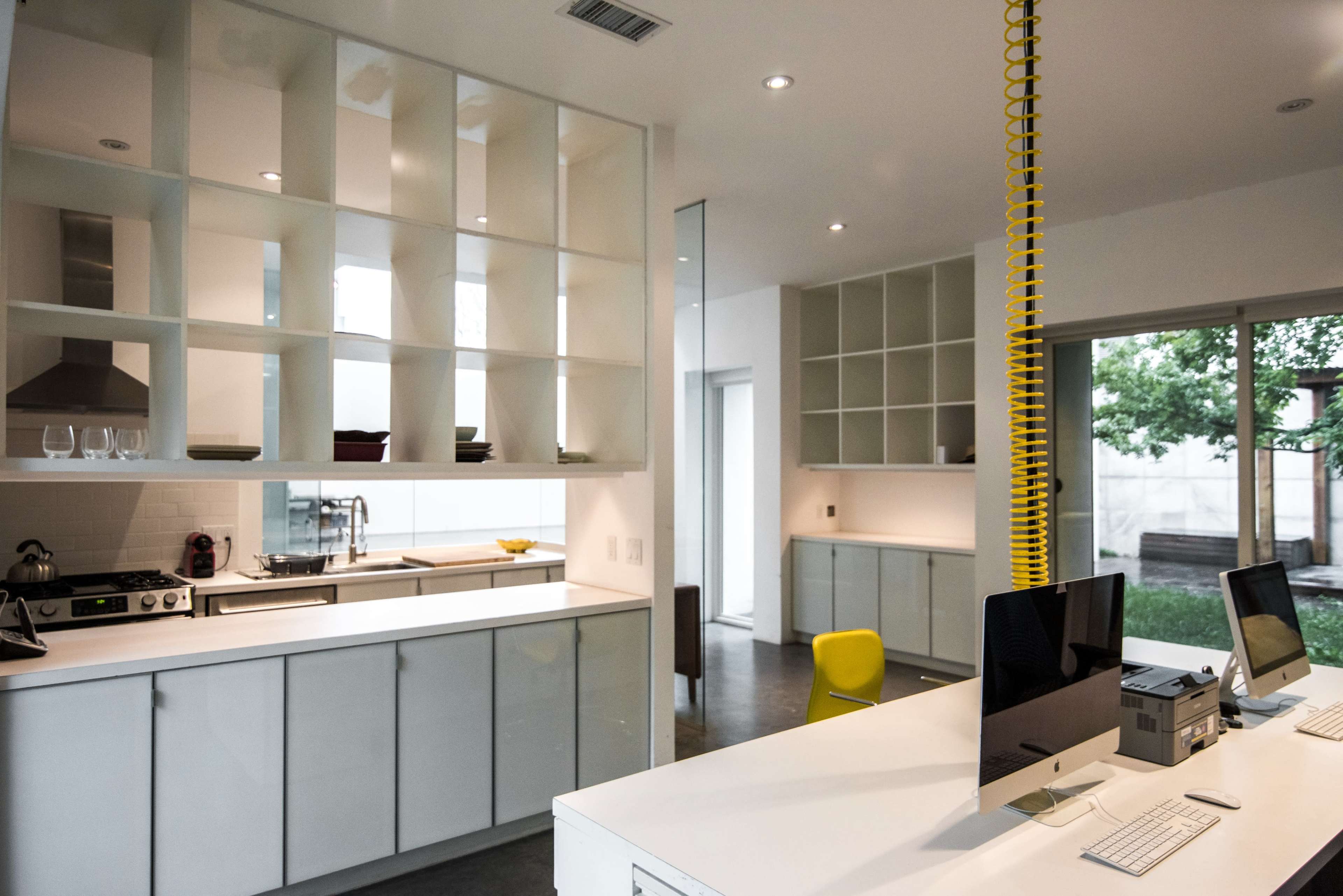 A modern kitchen features sleek white cabinetry, a central island with bar seating, and large windows that overlook a garden.