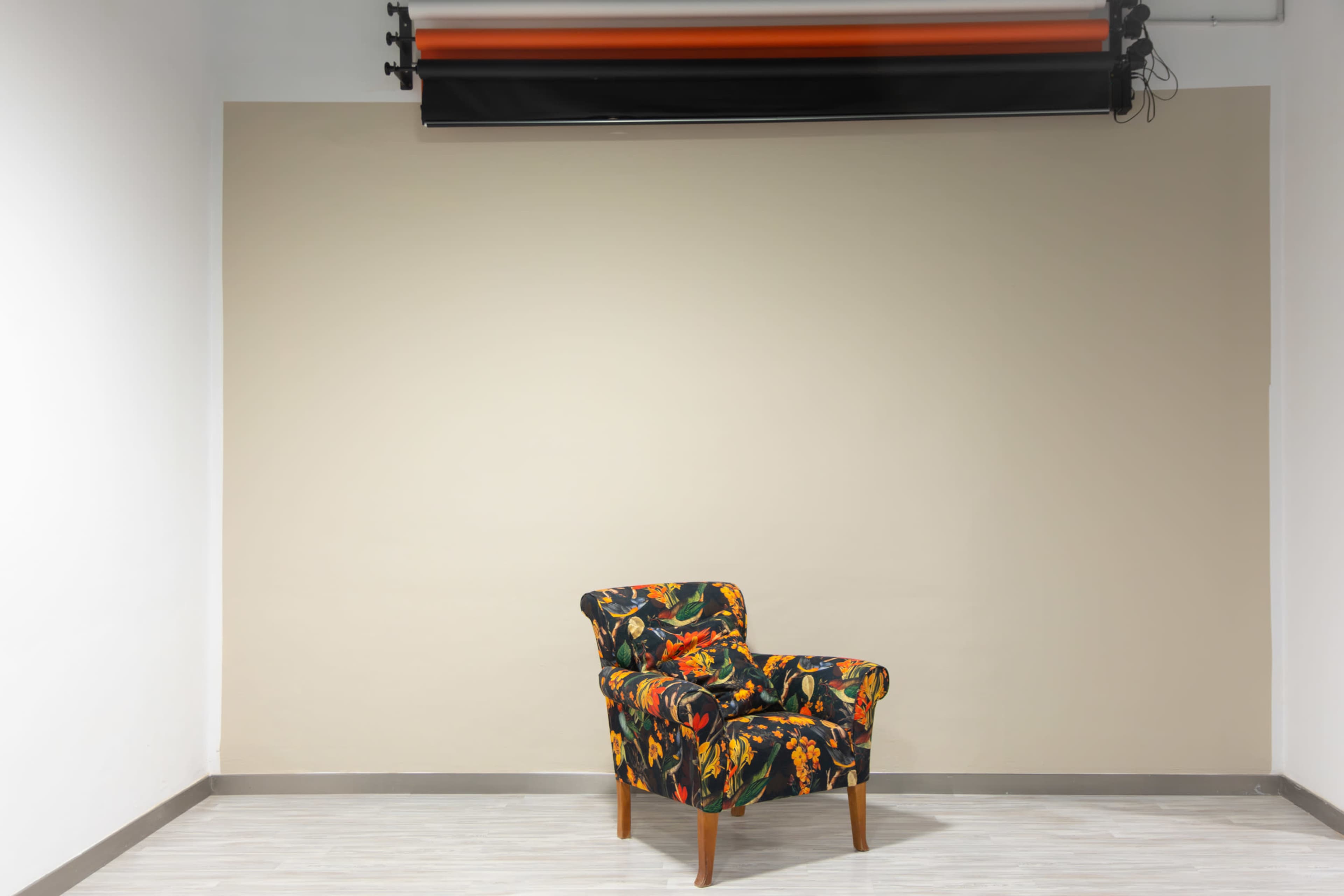 A colorful upholstered chair sits alone against a blank beige wall in a sparse room.