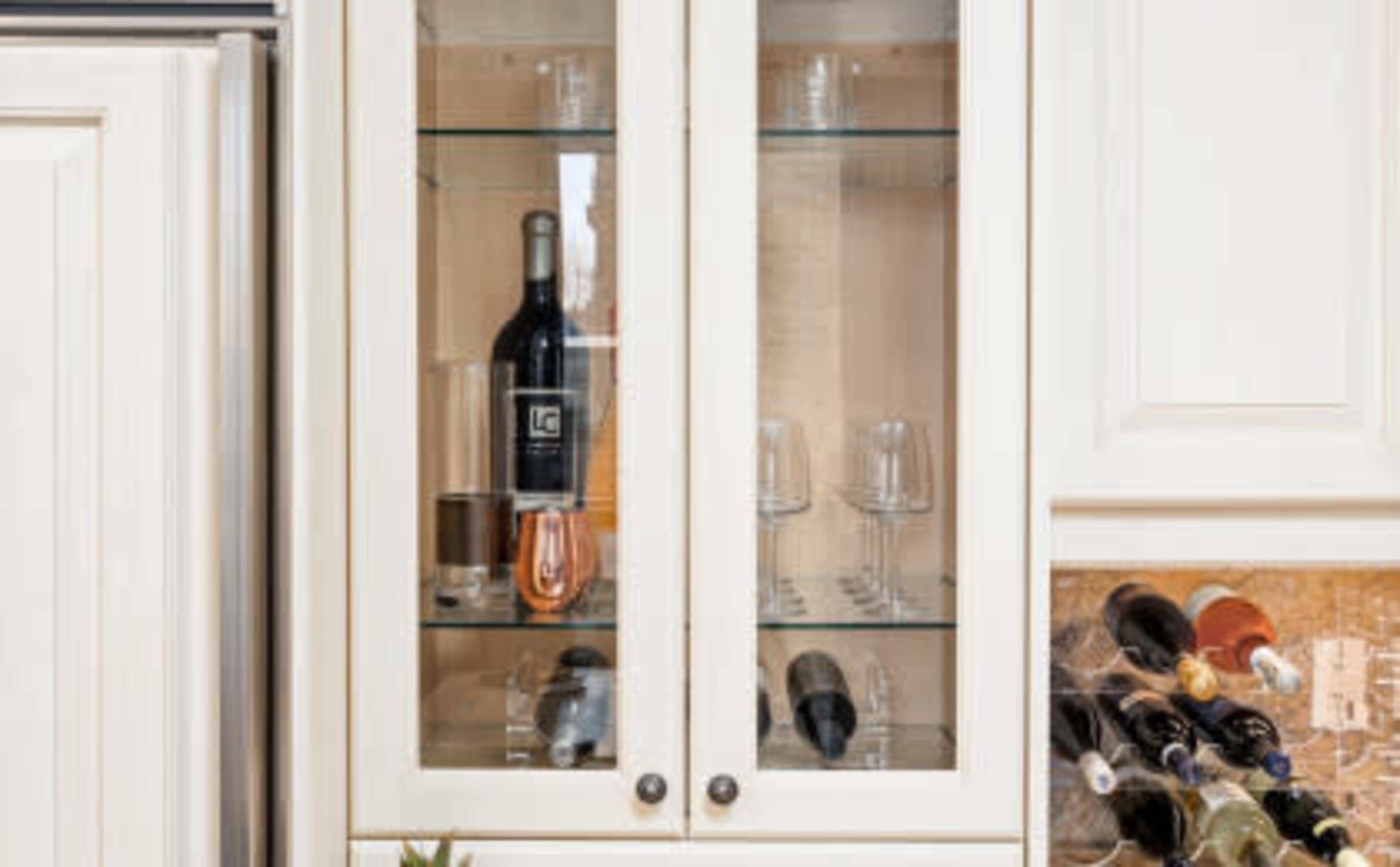 A glass-front cabinet displays several wine bottles and drinking glasses.