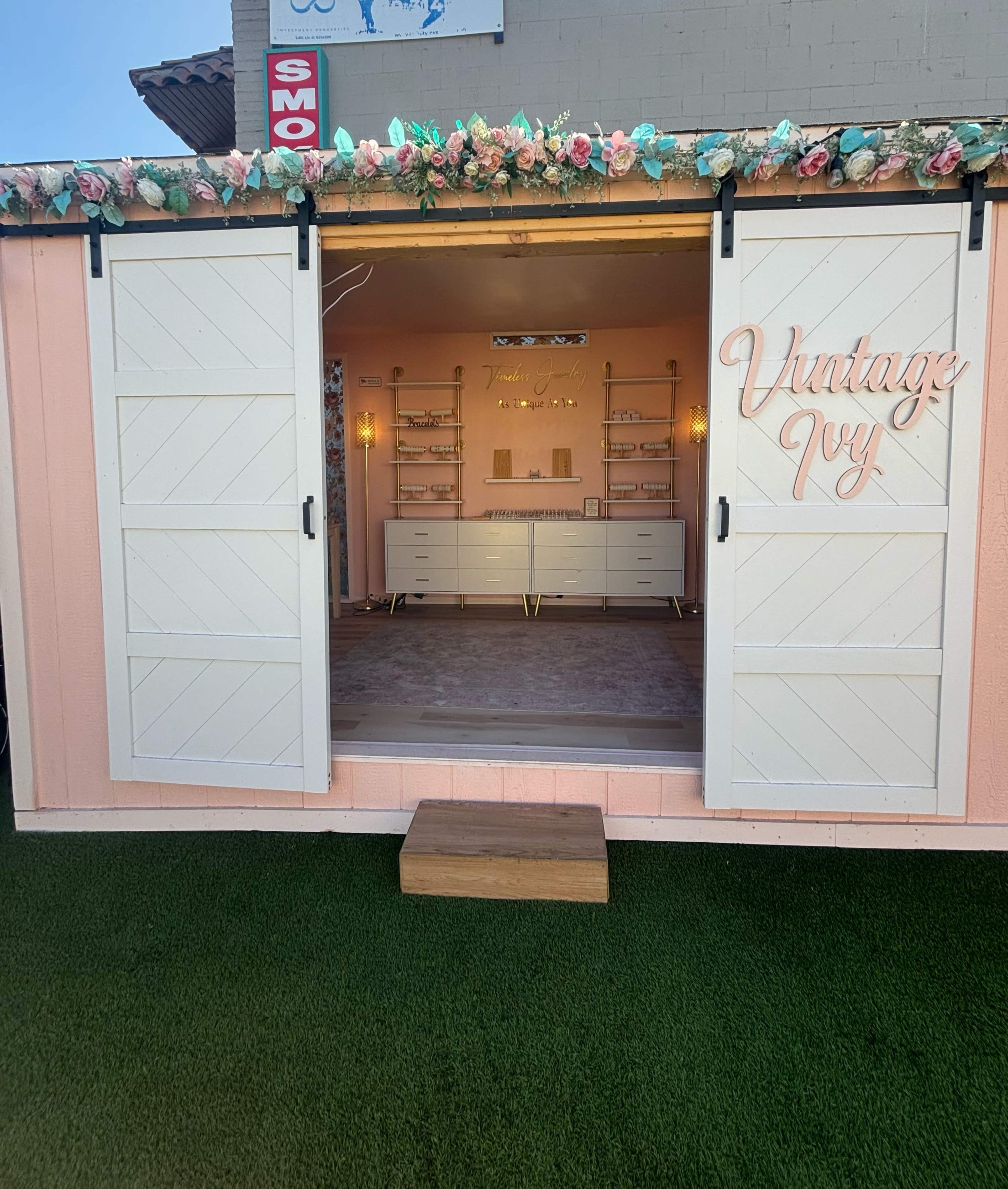 A brightly colored storefront with open white doors, revealing a neatly arranged interior adorned with floral decorations and a sign that reads "Vintage Ivy."