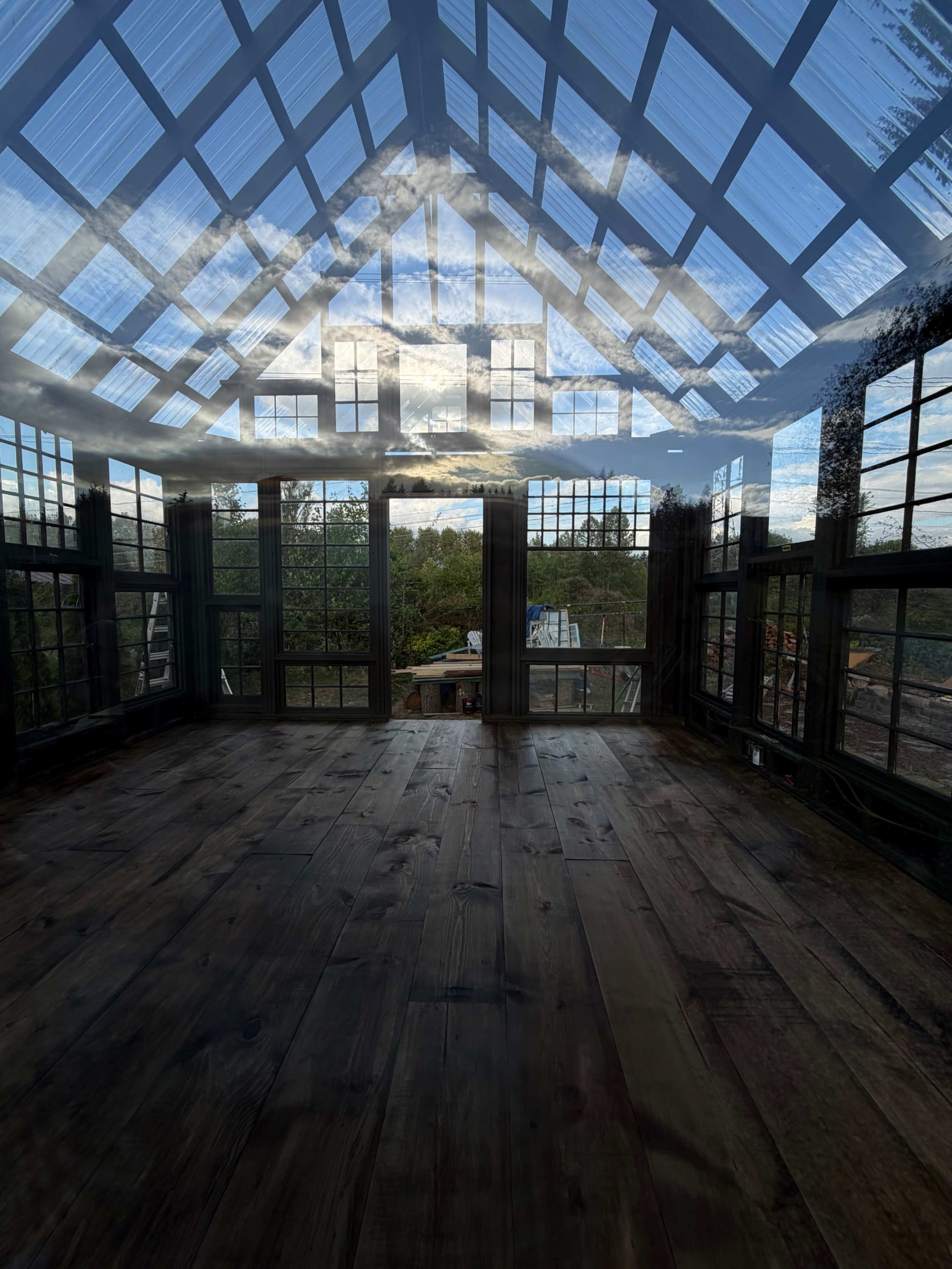 The image shows a spacious, sunlit room with large glass windows that reflect the sky and surrounding greenery.
