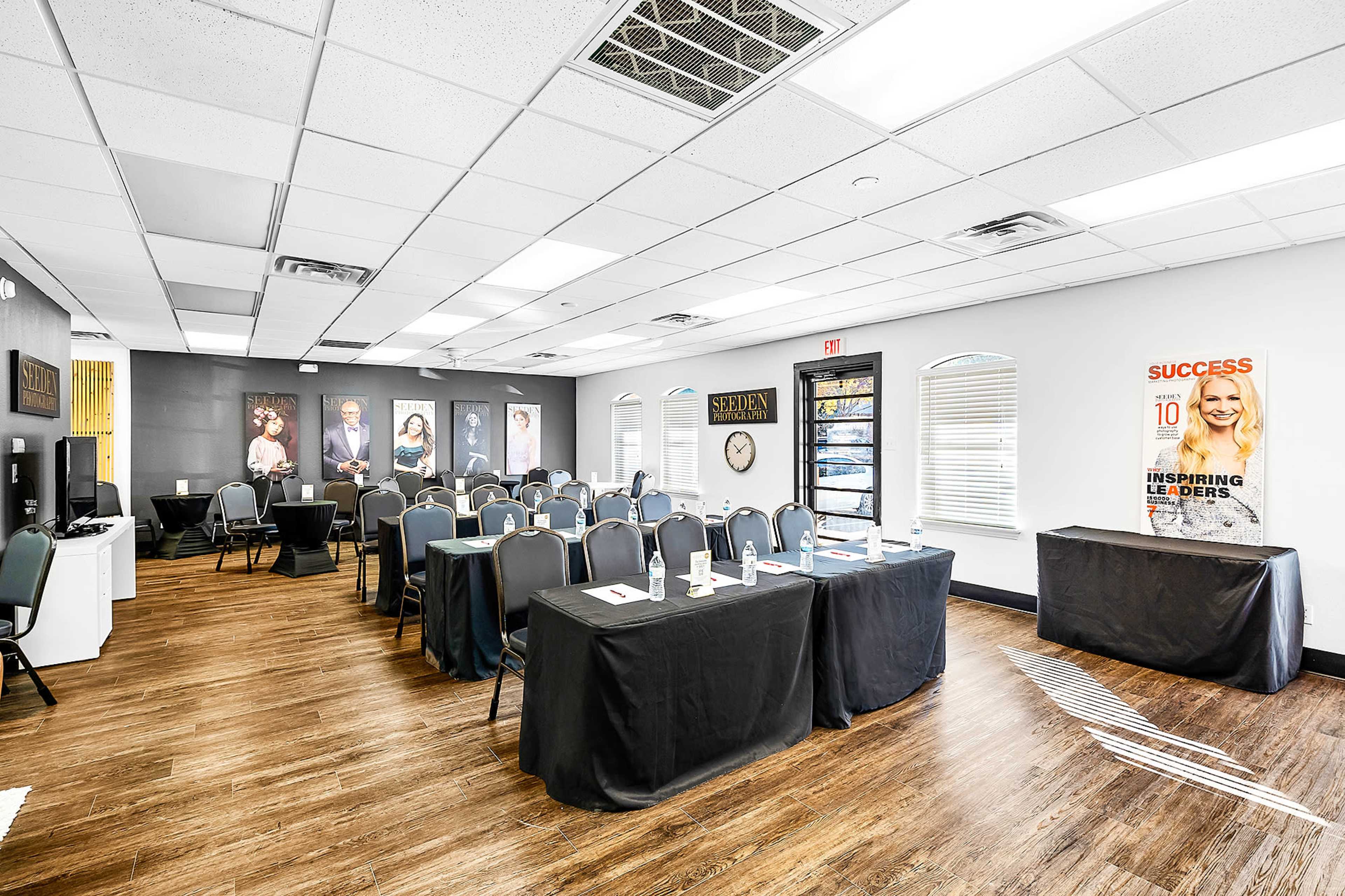 A meeting room set up with rows of chairs and tables, featuring a black tablecloth, wall decor, and large windows providing natural light.