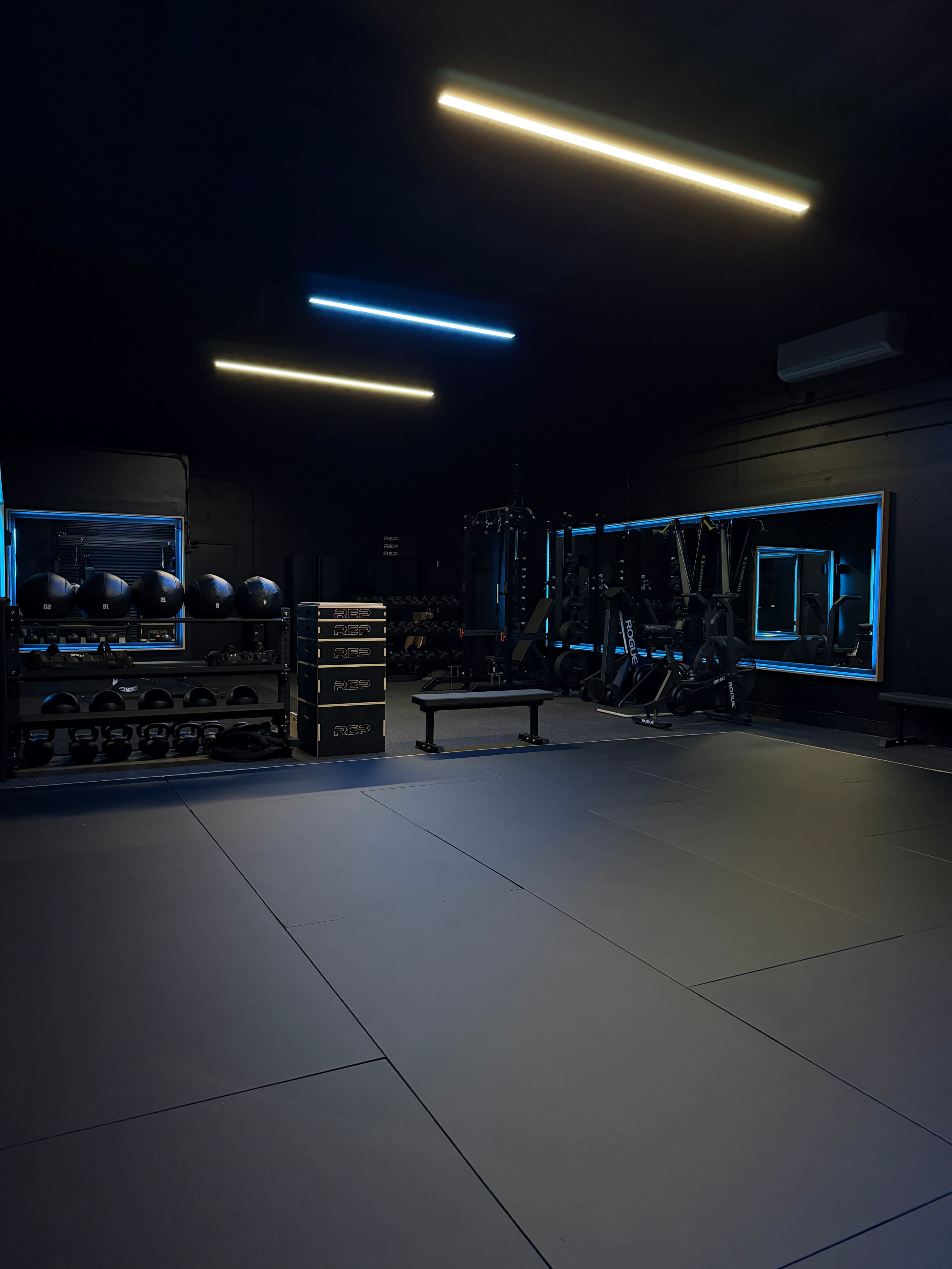 The image shows a modern gym interior with black walls, exercise equipment, and blue LED lighting.
