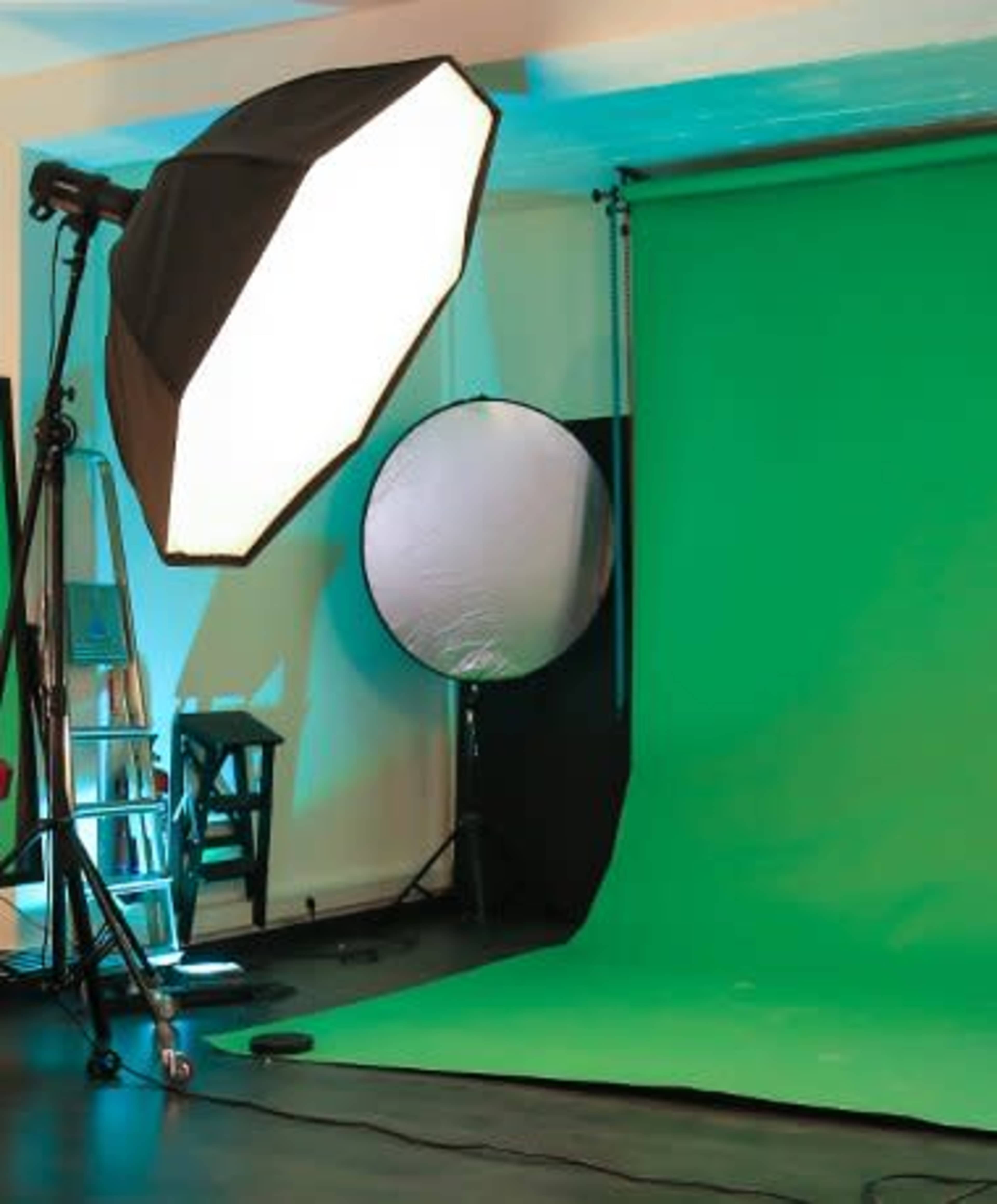 The image shows a photography studio setup featuring a green backdrop, a large softbox light, and a reflective disc.