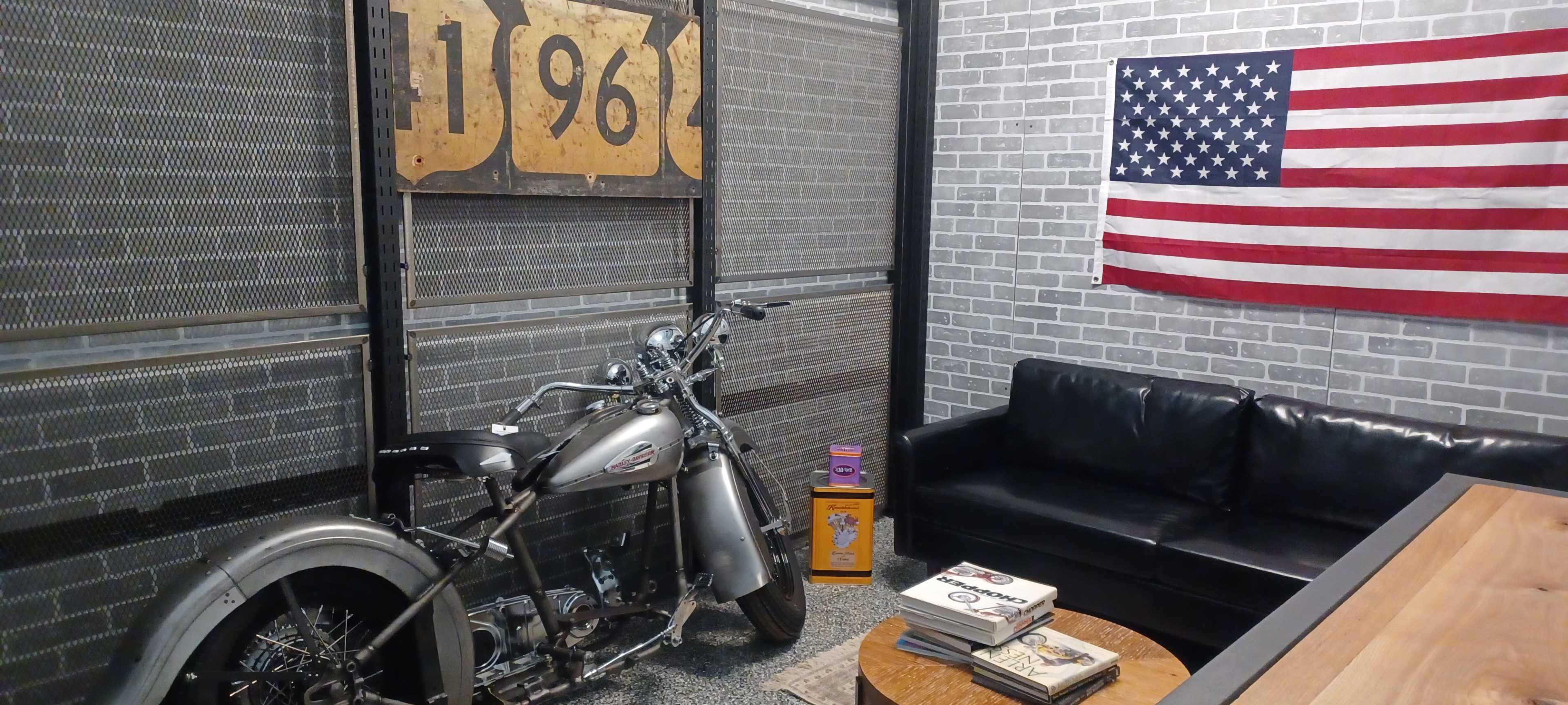 A vintage motorcycle next to a black sofa and a wooden coffee table, with an American flag hanging on the wall behind them.
