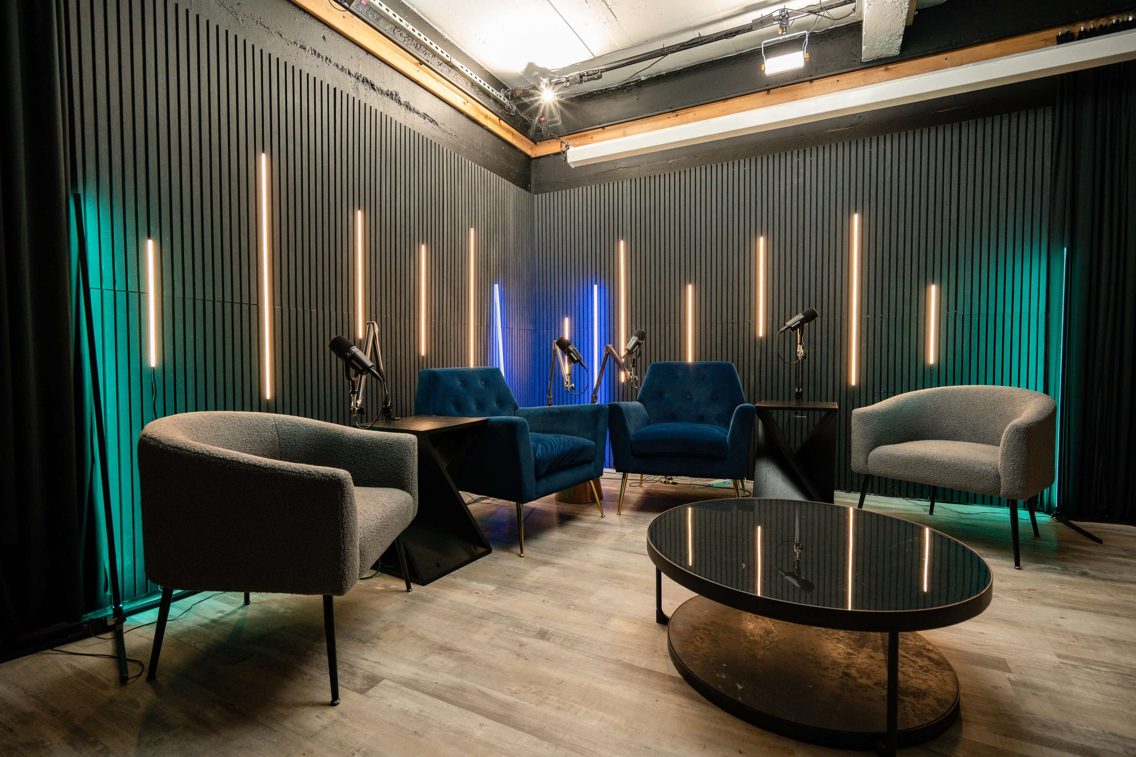 The image shows a modern lounge area with four chairs, a coffee table, and illuminated vertical light strips on the walls.